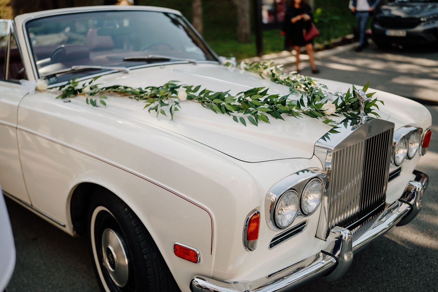 Classic white Rolls Royce decorated with greenery garland for a wedding ceremony.