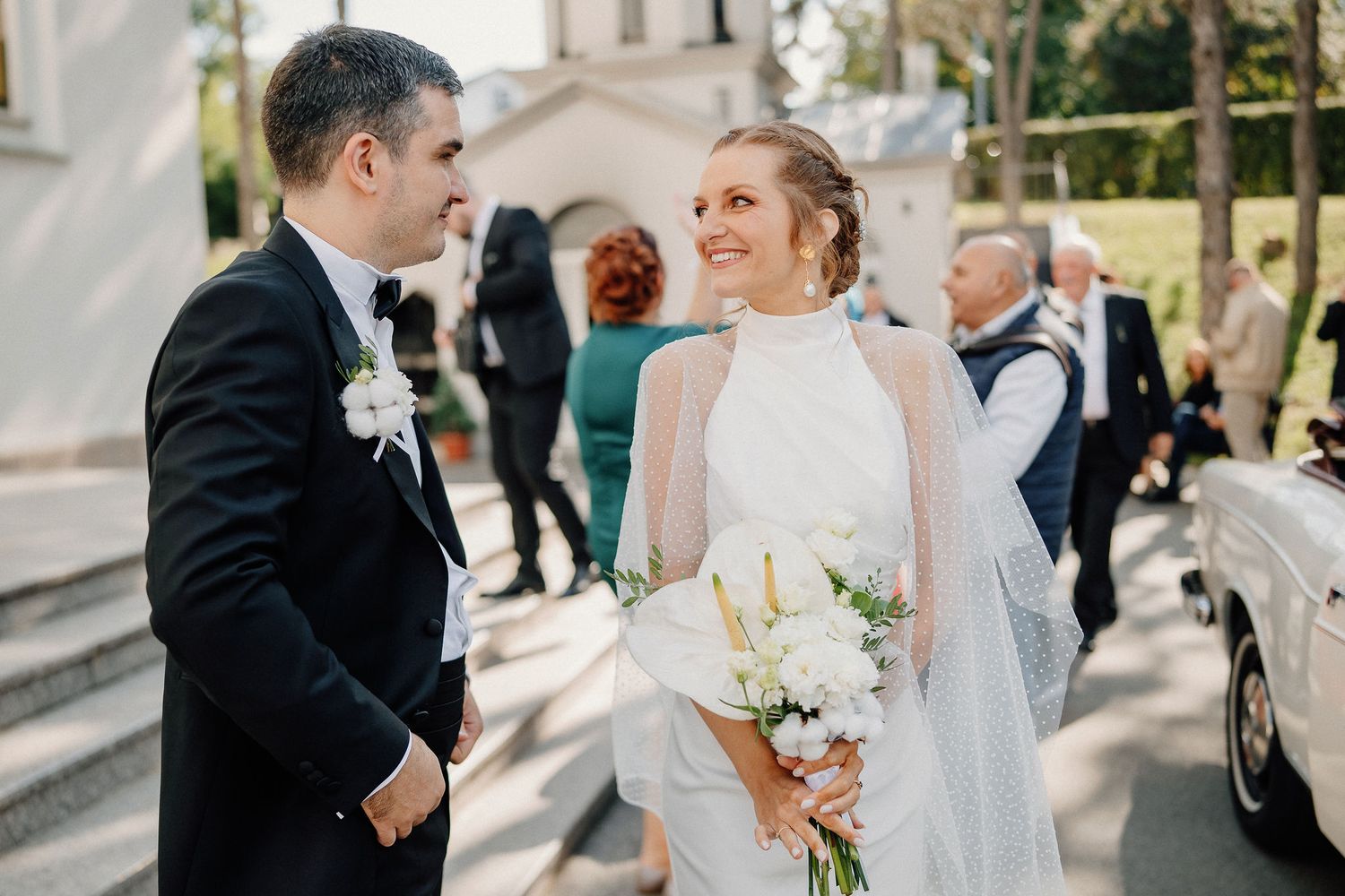 Newlywed couple shares intimate moments during outdoor wedding ceremony with white floral bouquet and formal attire.
