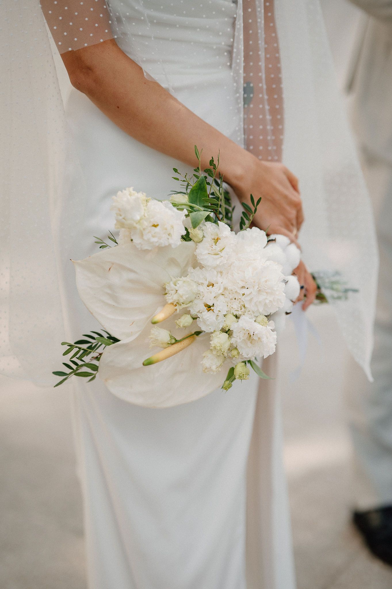 White floral bouquet with delicate petals and greenery held against a flowing white dress.