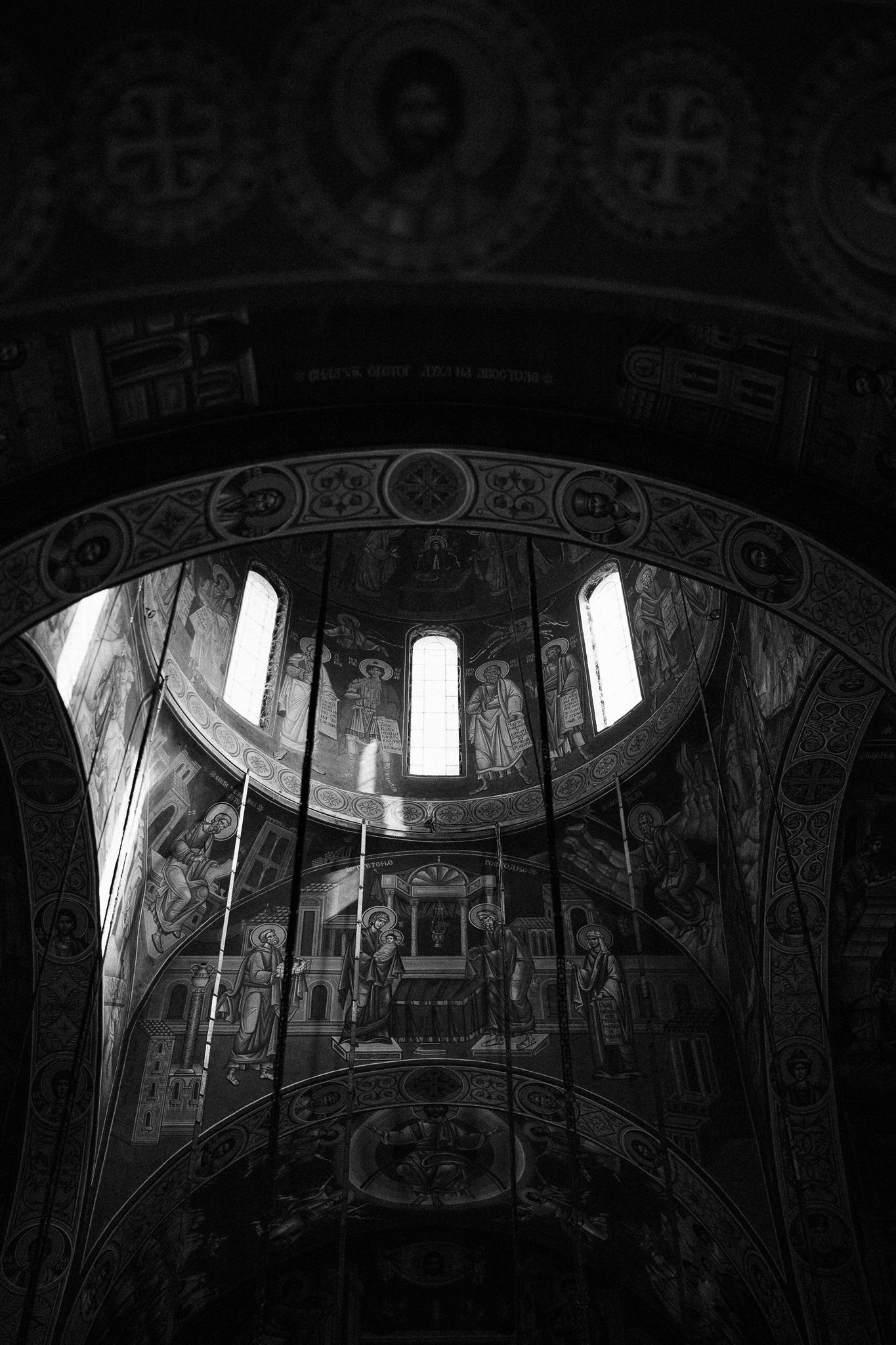 Ornate church interior with dramatic lighting streaming through windows illuminating decorative ceiling frescoes and arches.