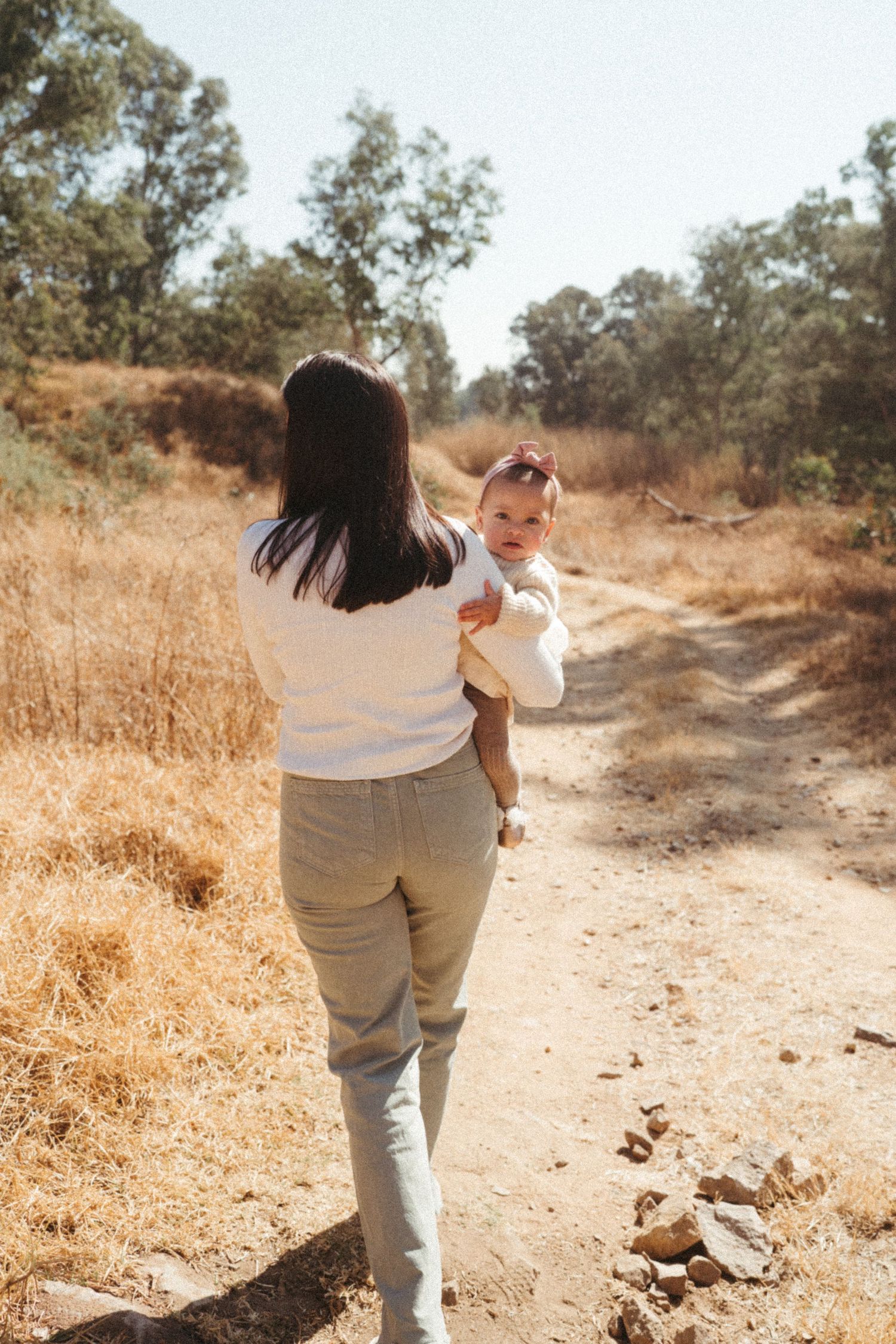 Parent and child walking together on dirt path through autumn landscape.