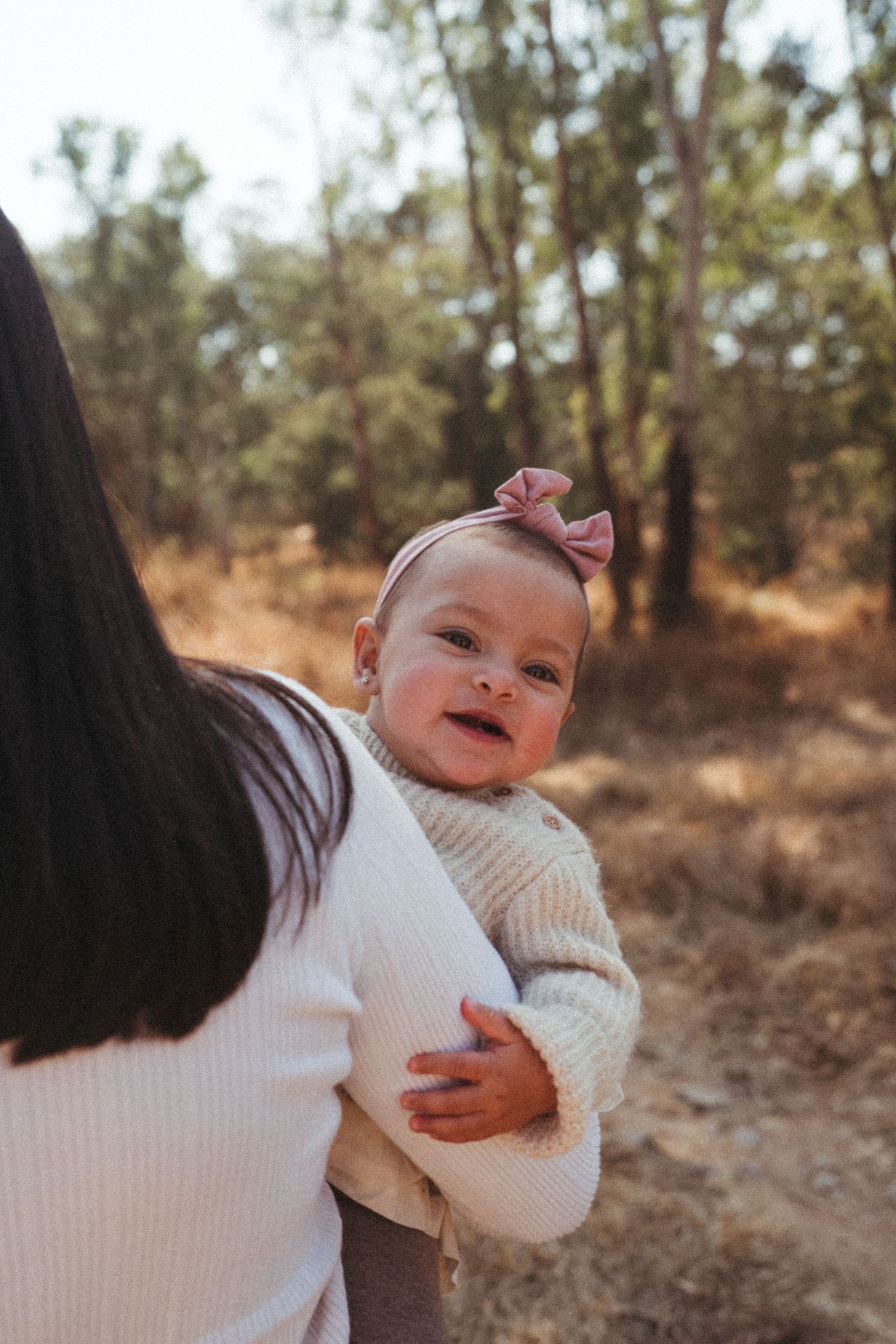 Baby in white sweater smiling during outdoor family photoshoot.