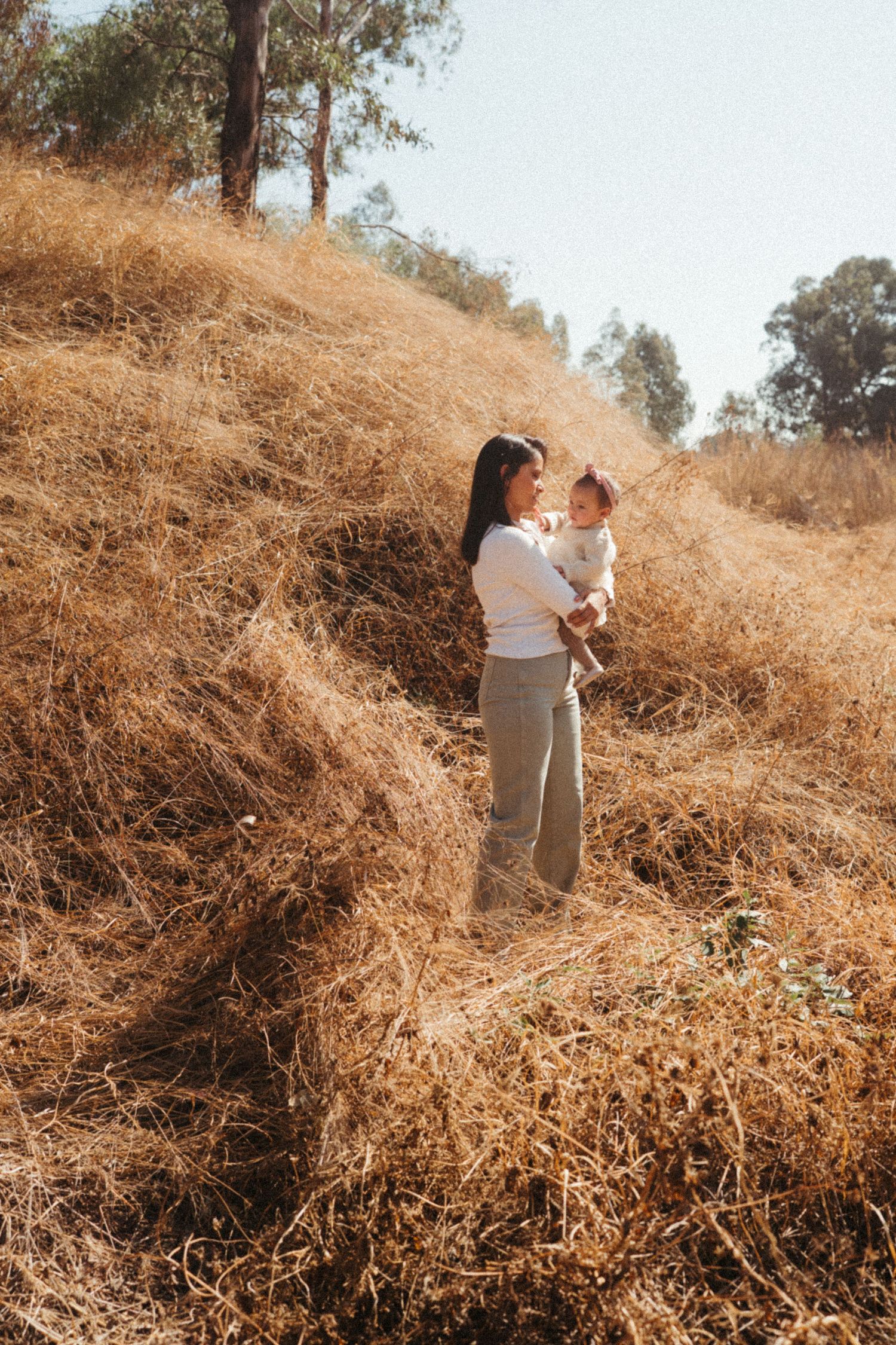 Playful family photoshoot on a sun-drenched hillside with dried grass.
