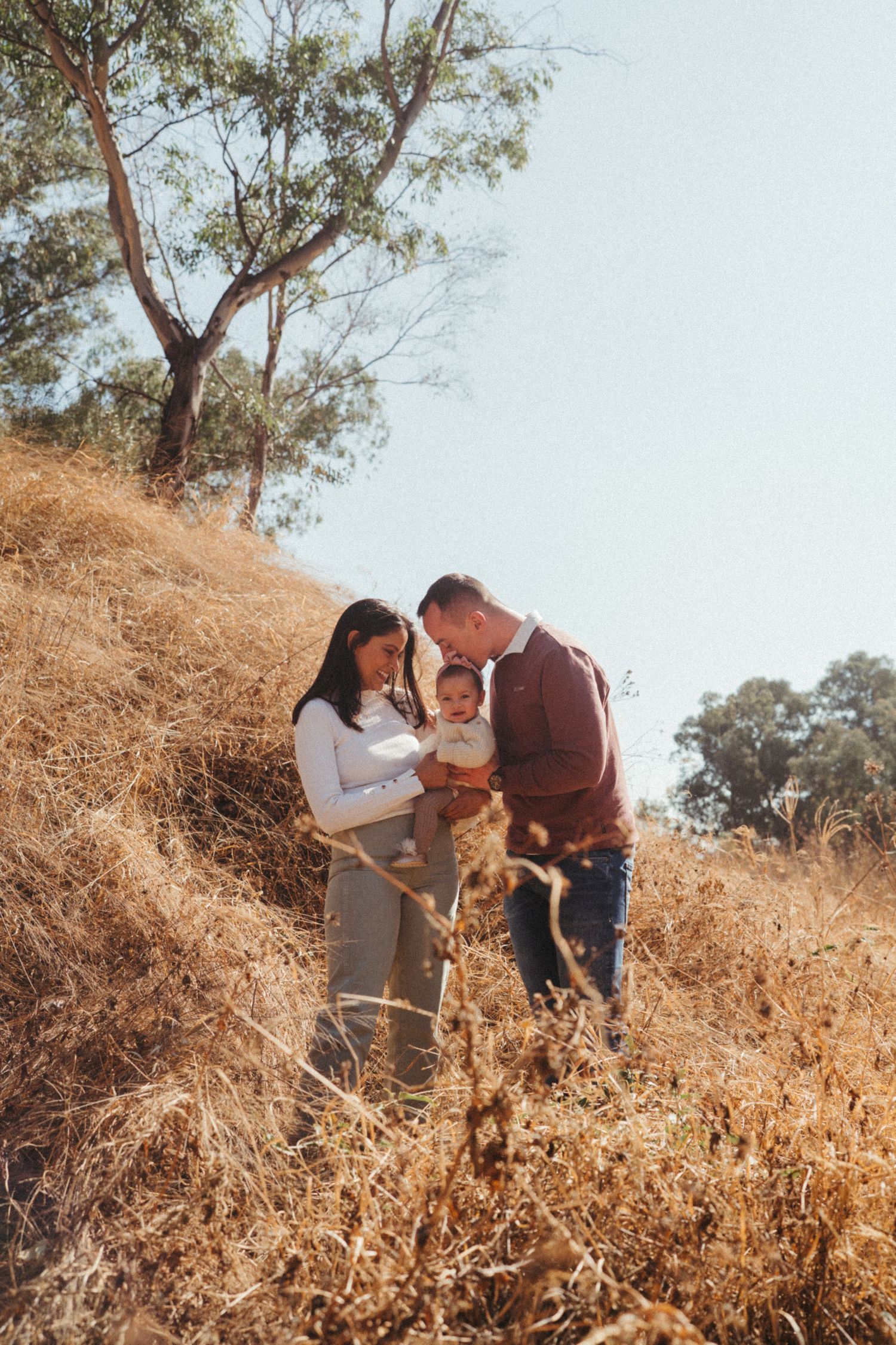 Family bonding moment captured against a backdrop of golden grass and trees.