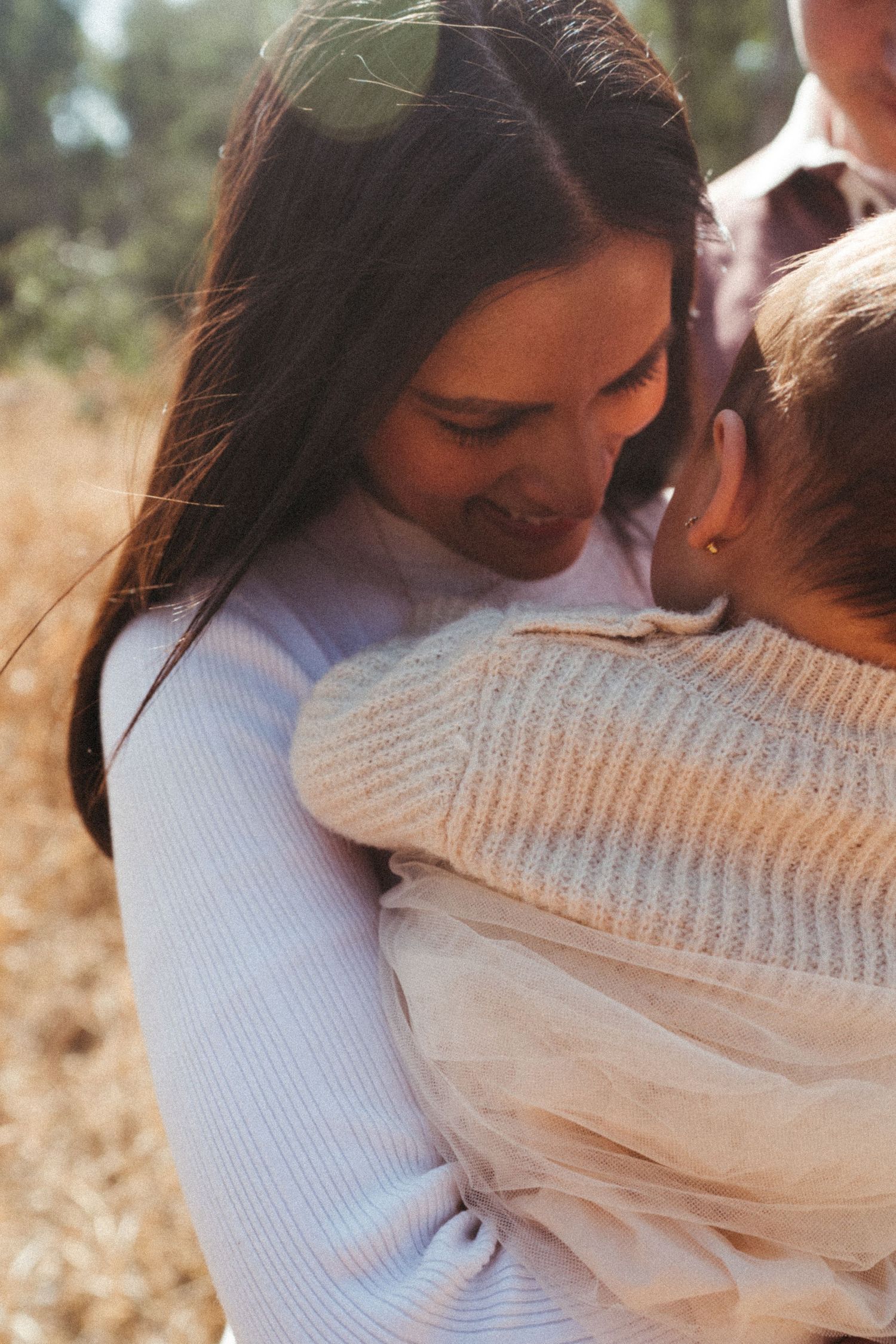 Close-up shots of gentle embraces between family members in white sweaters outdoors.