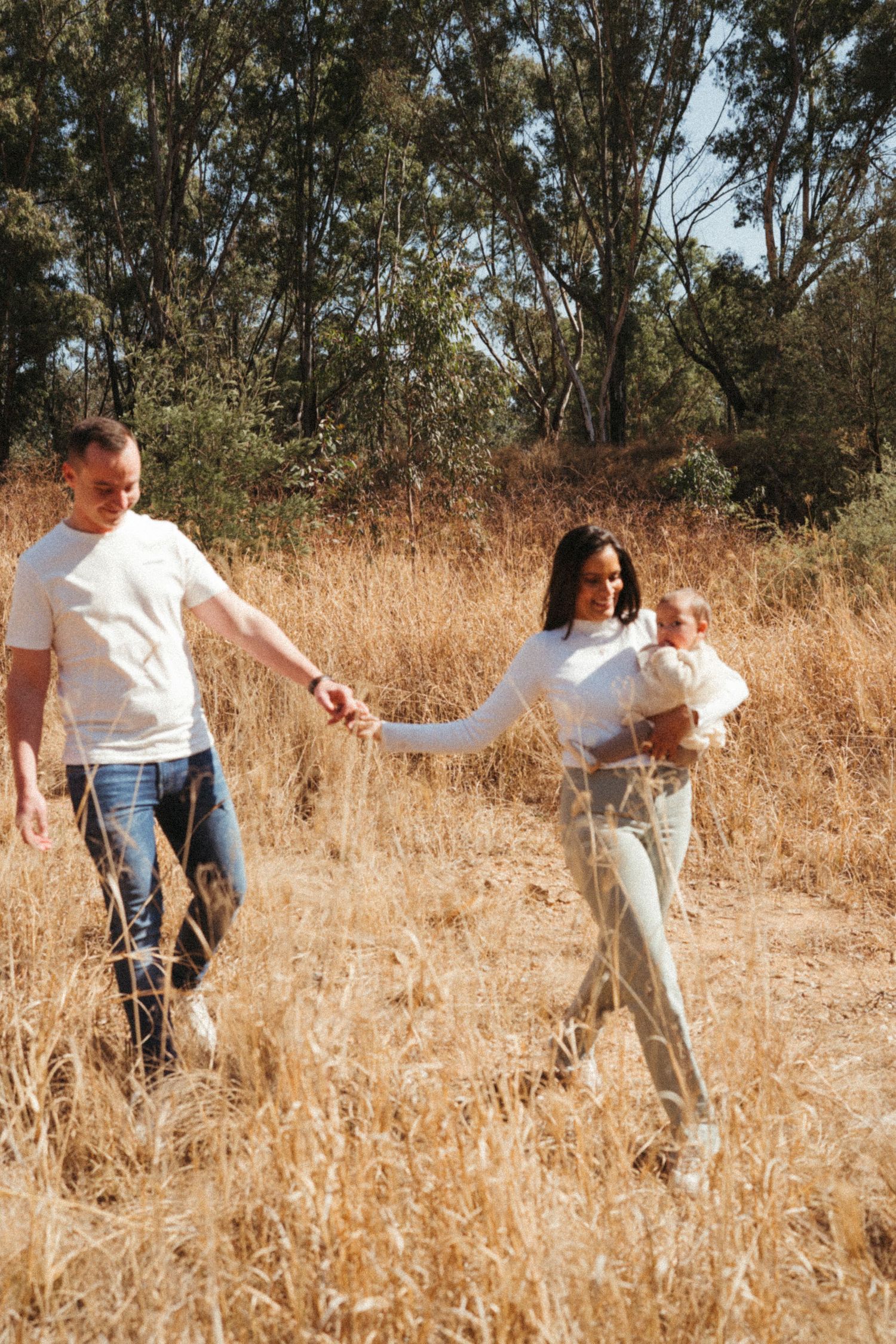 Family walking together through tall golden grass in a wooded area.