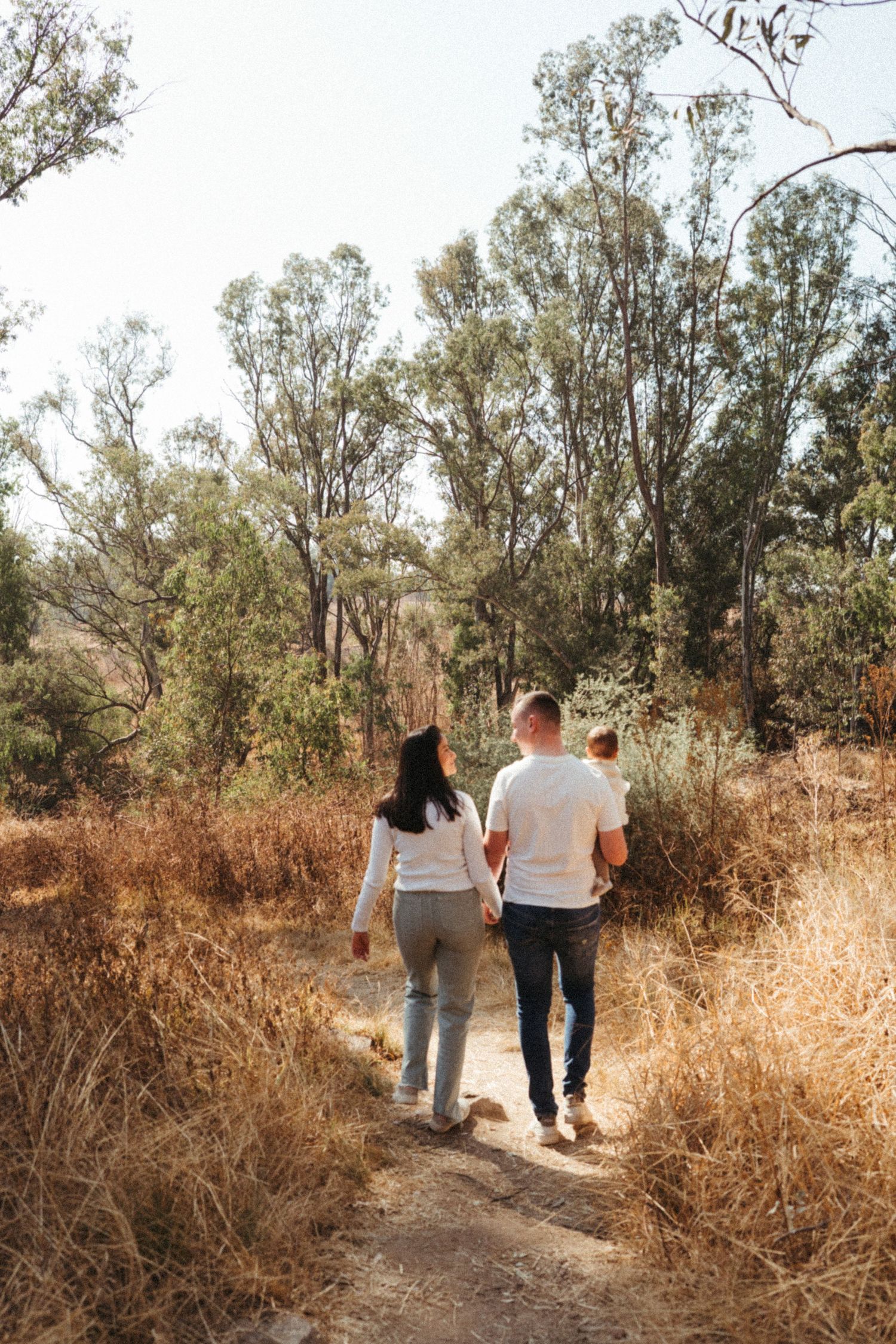 Family walking along a nature trail surrounded by dried grass and eucalyptus trees.