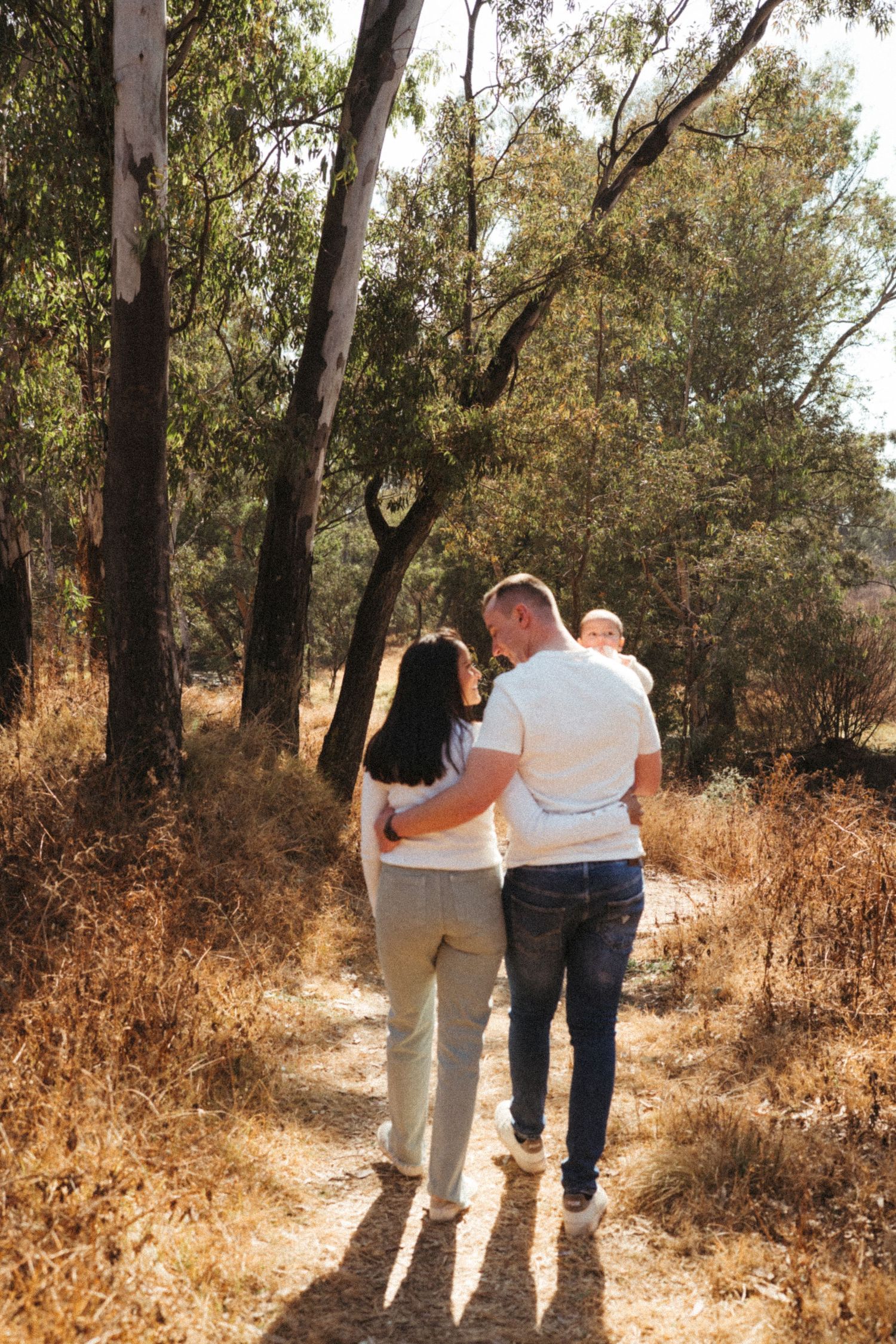 Family walking together on a sunlit path through eucalyptus grove.