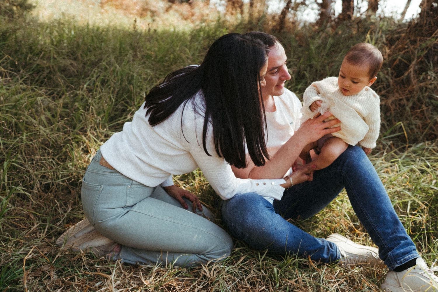 Tender family moment captured in a grassy field during golden hour.