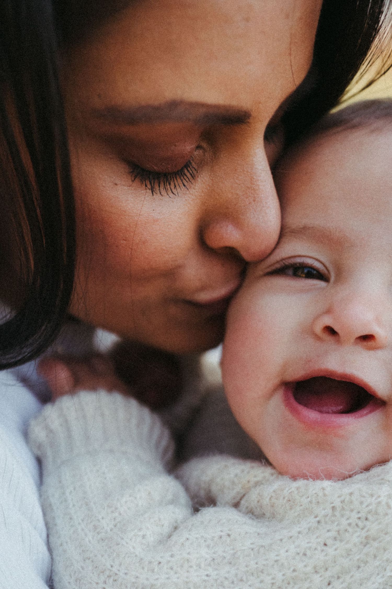 Close-up series of loving kisses and cuddles with baby wearing white knit sweater.