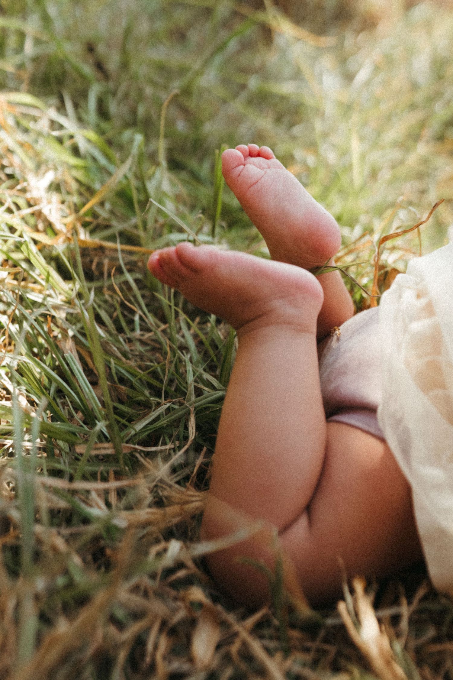 Close-up of tiny bare feet resting on dried grass and leaves.