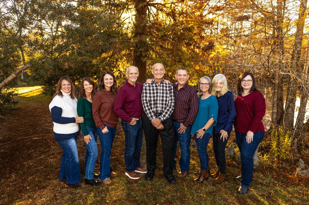 Group portrait of people in casual attire posed against fall foliage at sunset.
