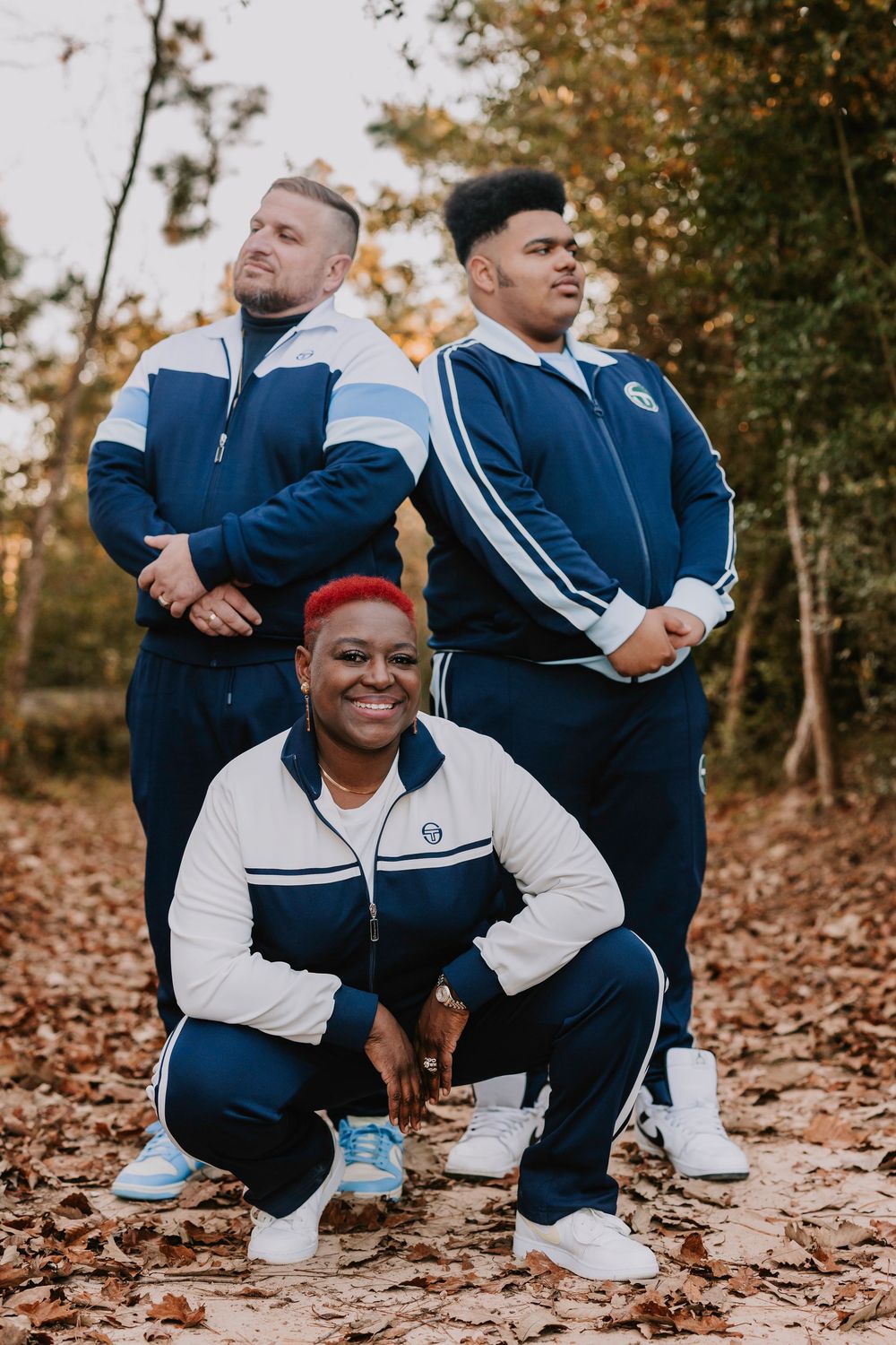 Three people in matching blue and white athletic wear pose together on fallen autumn leaves.
