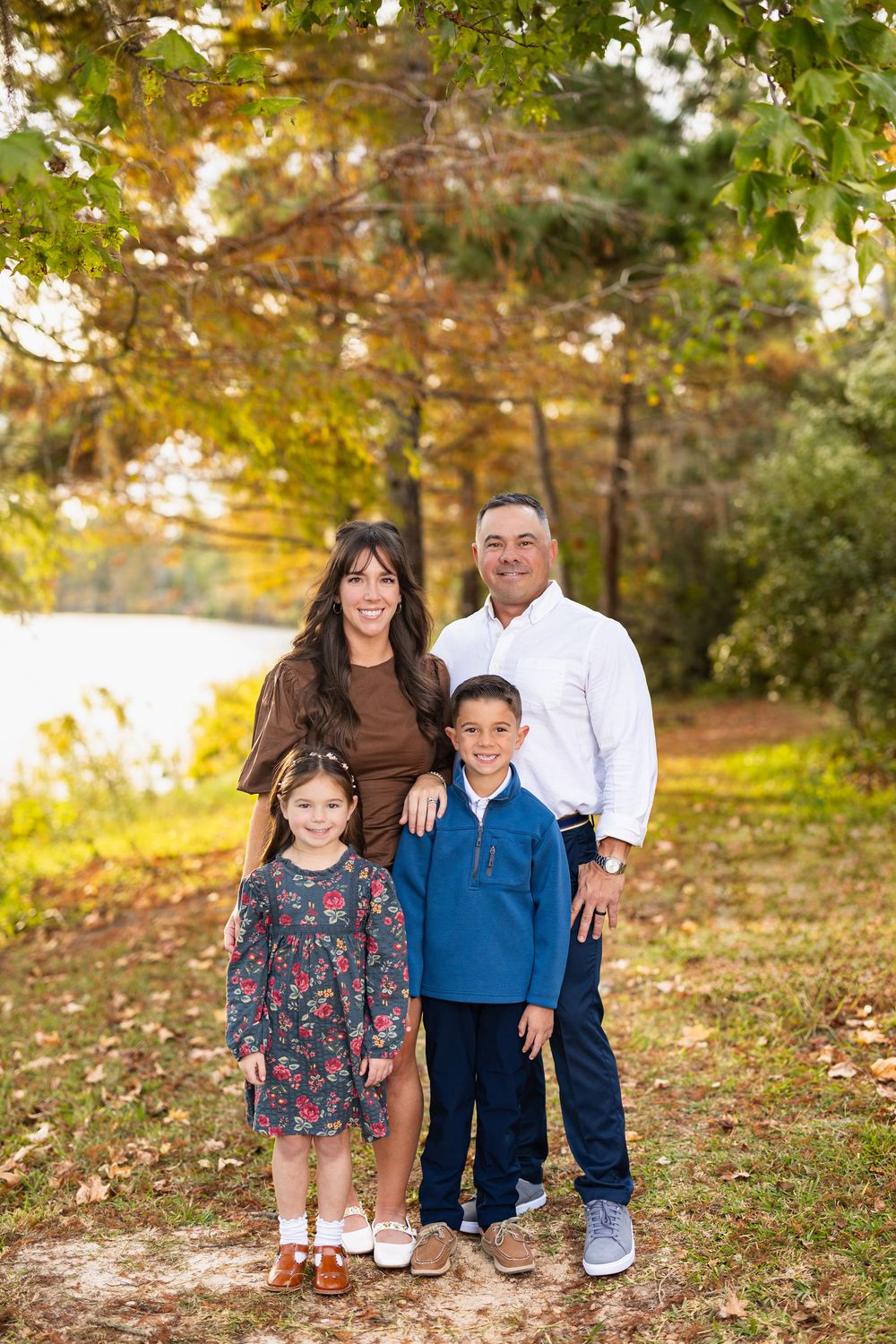 A family of four poses together on an autumn path with fall foliage in the background.