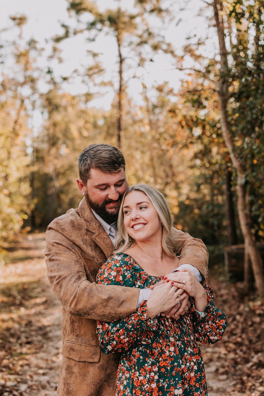 A couple embraces in a romantic autumn forest setting during golden hour.
