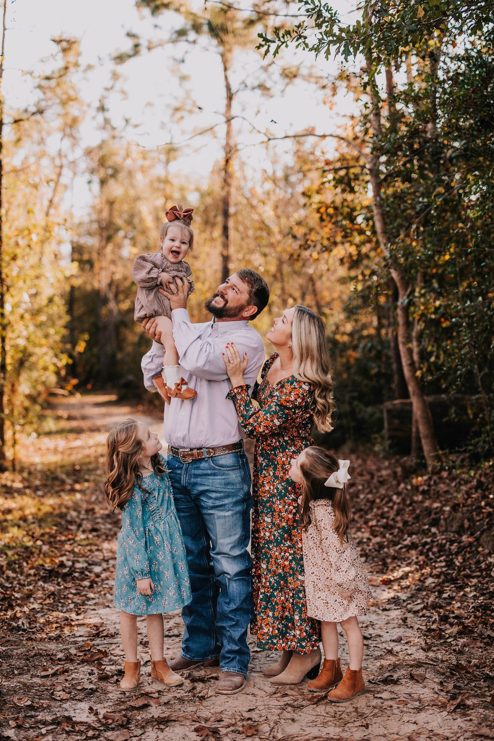 A family shares a tender moment together on a leaf-covered forest path.
