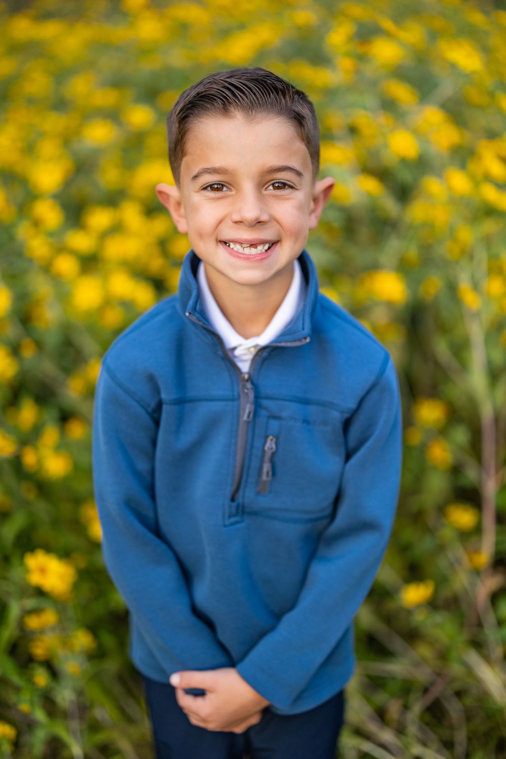 A child in a blue fleece pullover smiles at the camera with yellow flowers in the background.