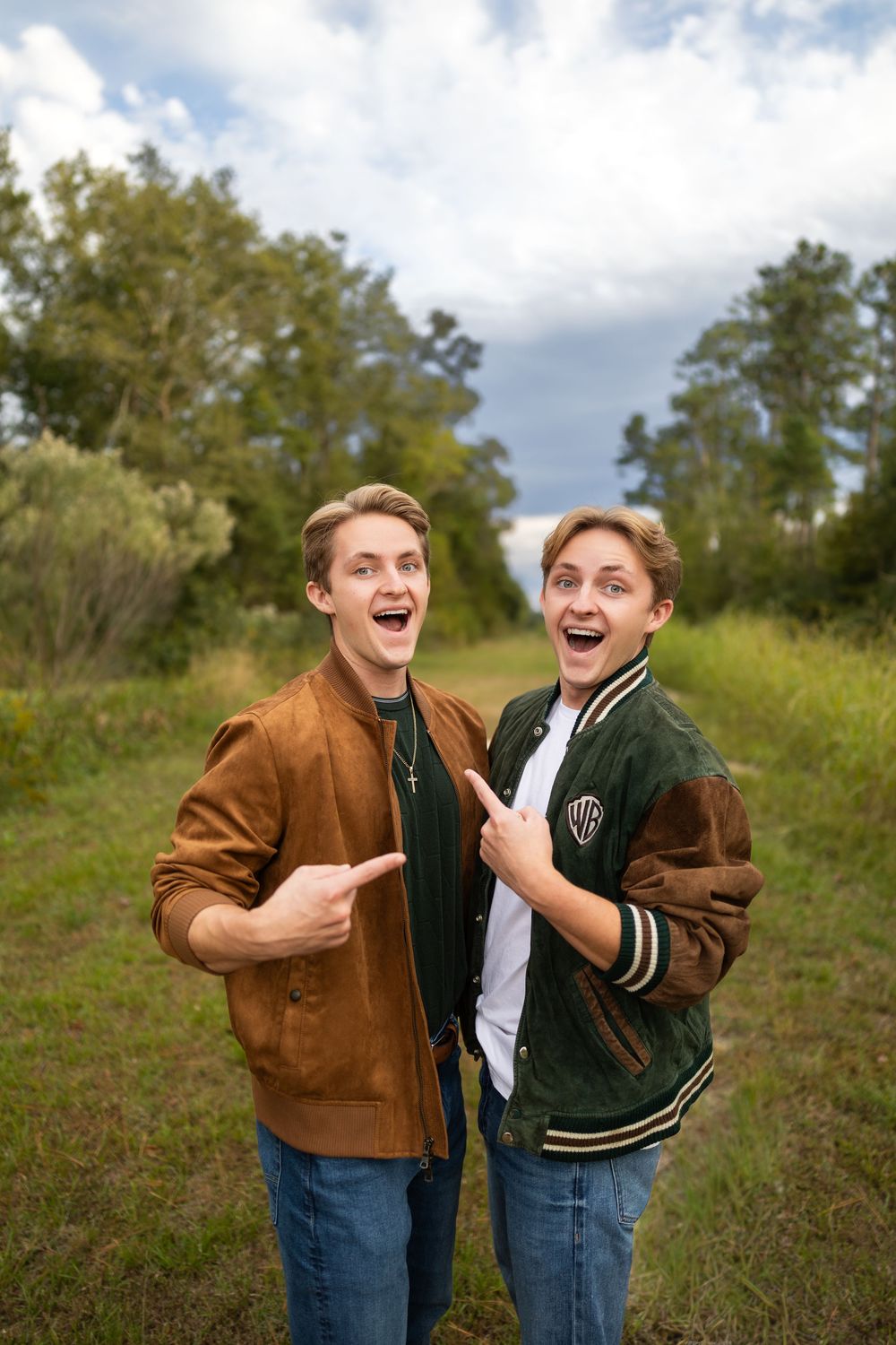 Two people in varsity jackets sharing an animated laugh together in a natural outdoor setting.