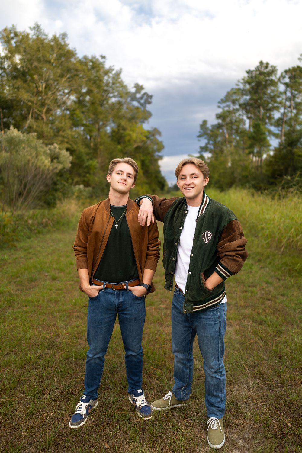 Two people in casual outfits striking fun poses in a grassy field under cloudy skies.