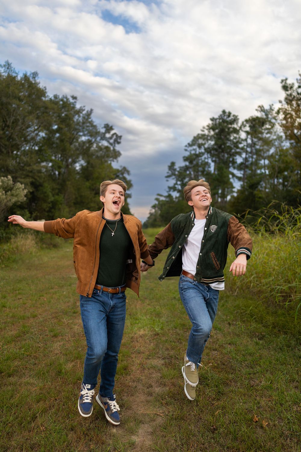 Two people jumping playfully on grassy hill during cloudy afternoon.