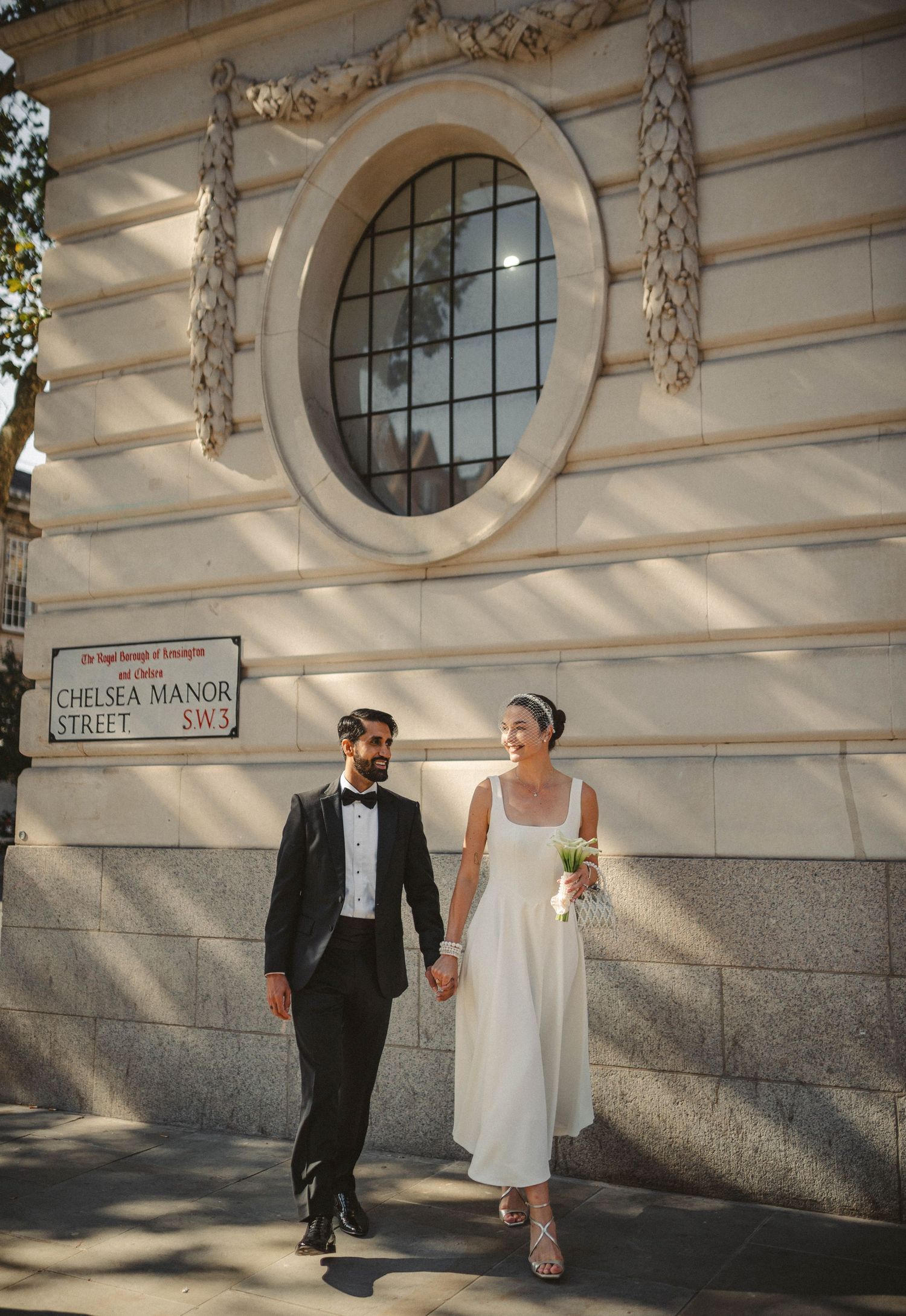 Wedding couple walking along Chelsea Manor Street with classic architecture.