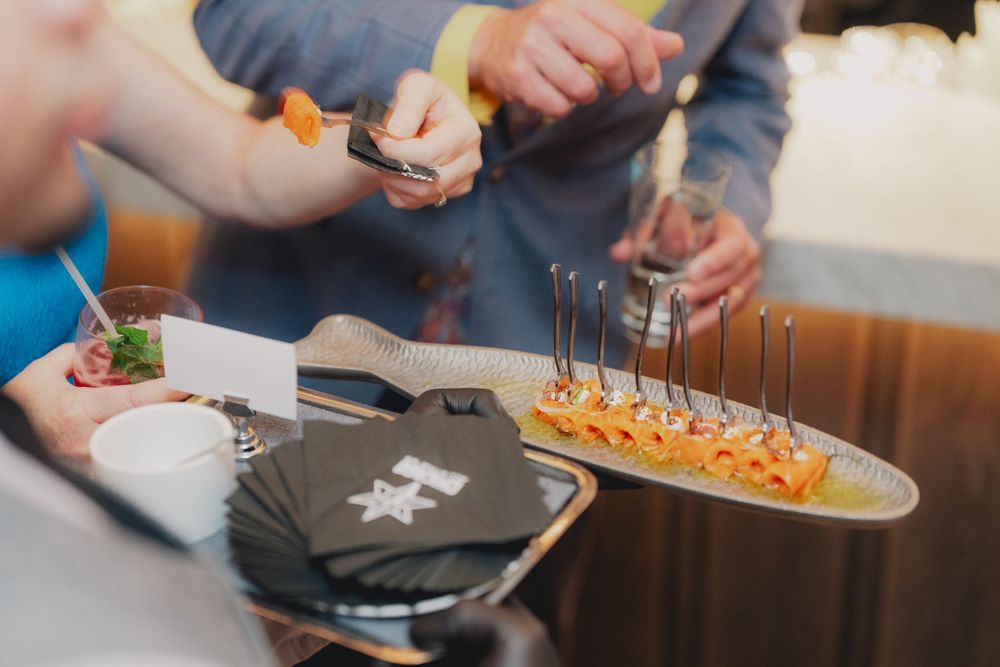 Guests serving themselves elegant canapés on a platter at a catered event with forks and small bites.