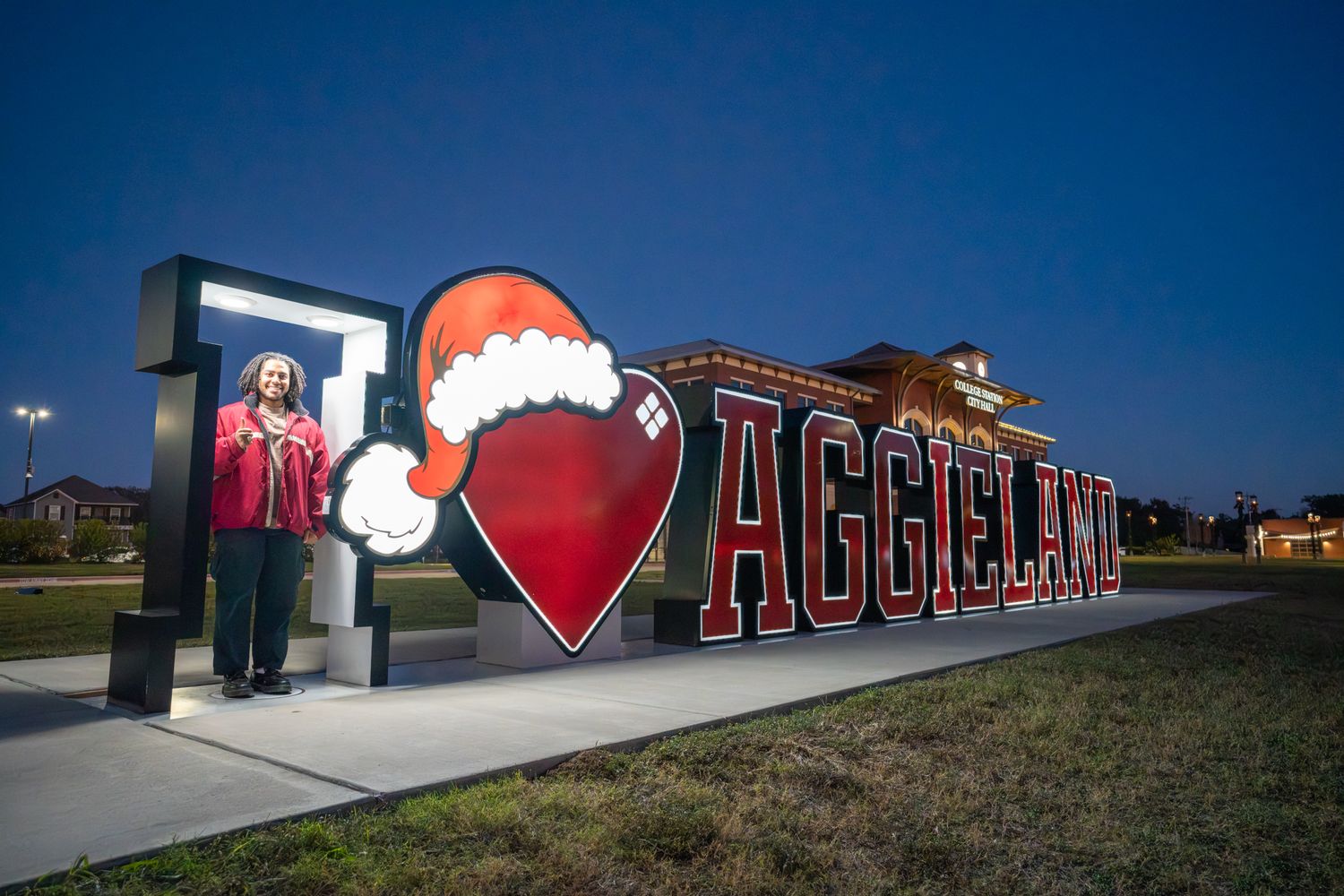 Large outdoor sign reading 'Aggies' with Santa hat decoration illuminated at night against dark blue sky.