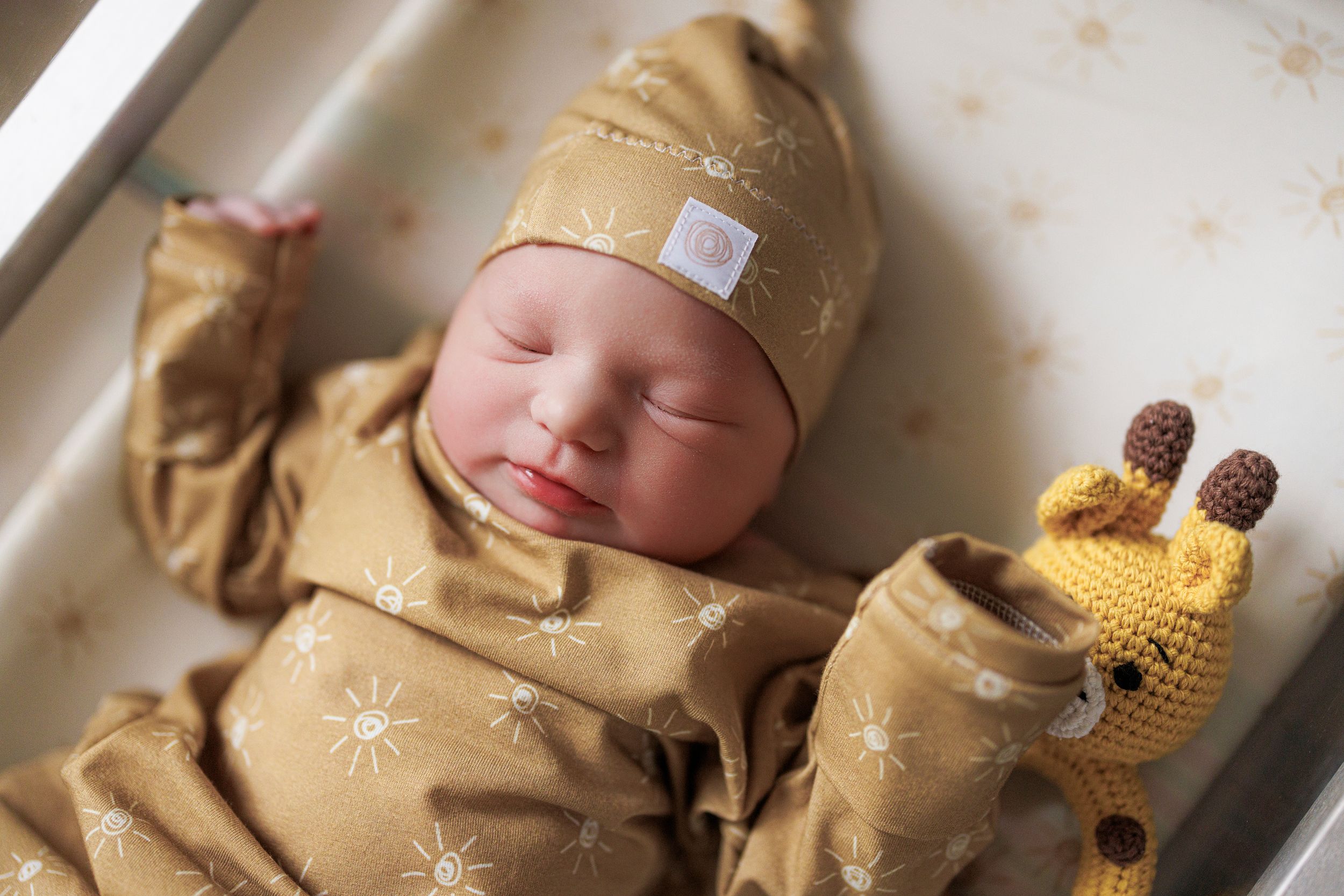 A sleeping newborn baby wearing a knitted yellow and brown giraffe-themed outfit and hat.