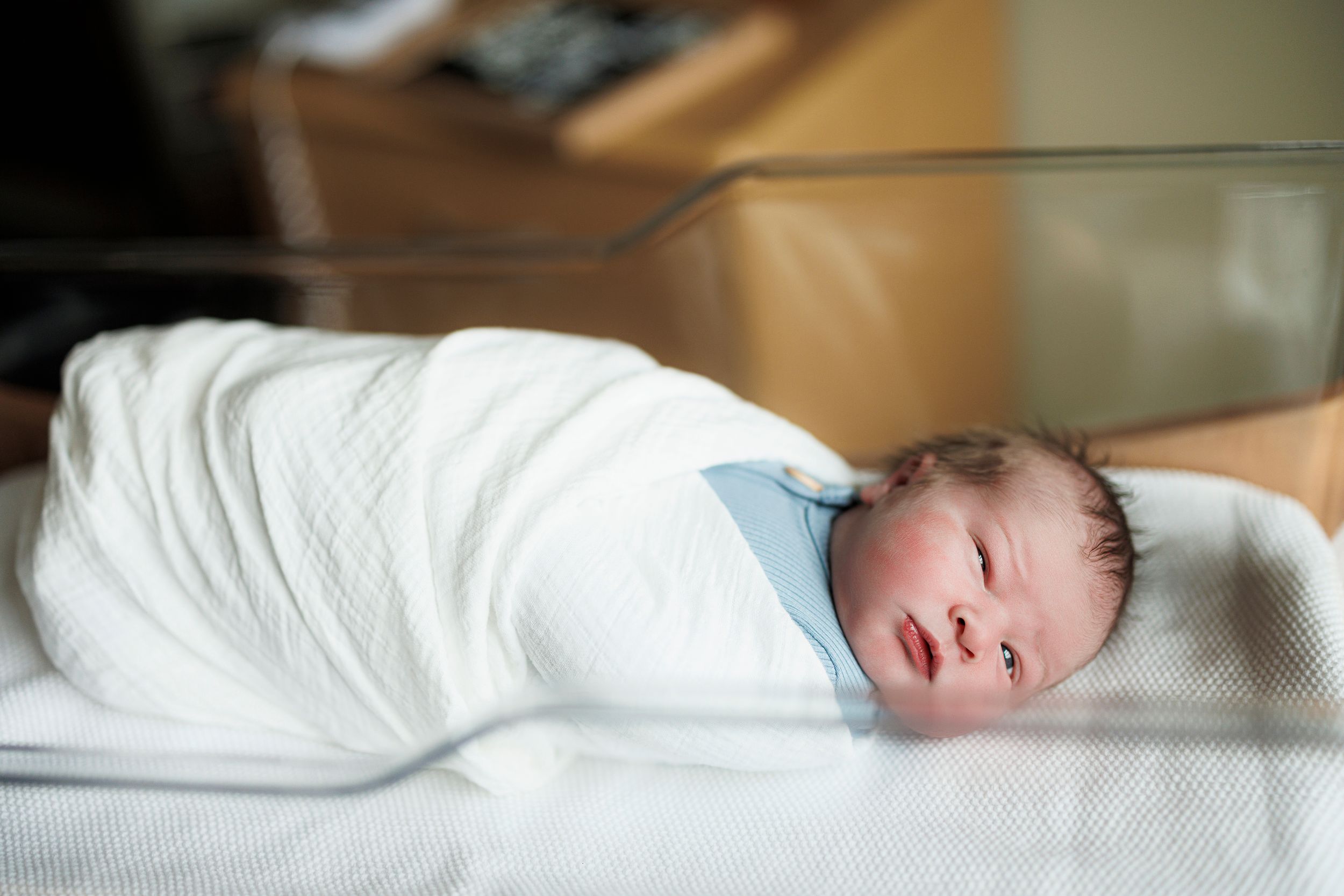 A sleeping newborn baby swaddled in white blankets rests peacefully on a soft surface.