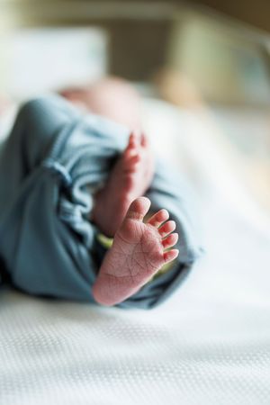 Close-up view of tiny baby feet against a white textured background with gentle lighting.