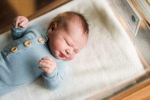 A sleeping newborn baby rests peacefully on a white textured blanket in soft natural light.