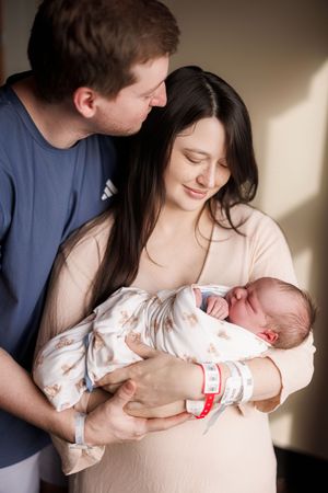 A tender moment as new parents cradle their newborn baby in a hospital room with soft lighting.