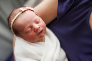 Newborn baby sleeping peacefully while swaddled in white blanket against dark blue background.