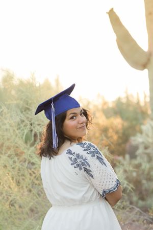 Light and airy senior photo of a girl smiling with her graduation cap on her head at Desert Botanical Garden in Phoenix, Arizona.
