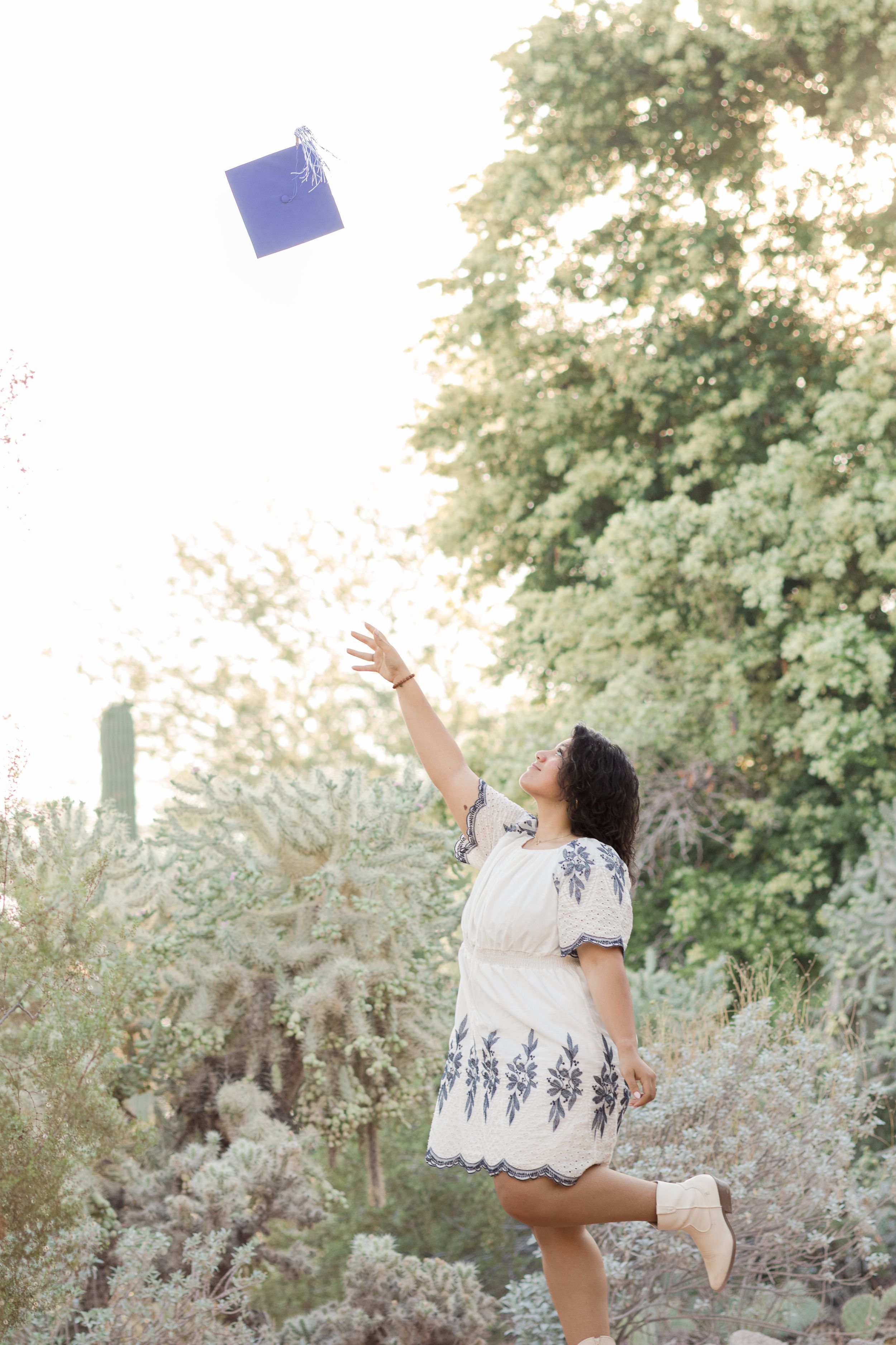 Light and airy senior photo of a girl throwing her graduation cap in the air at the Desert Botanical Garden in Phoenix, Arizona.