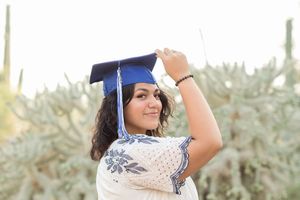 Light and airy senior photo of a girl smiling with her graduation cap on her head at Desert Botanical Garden in Phoenix, Arizona.