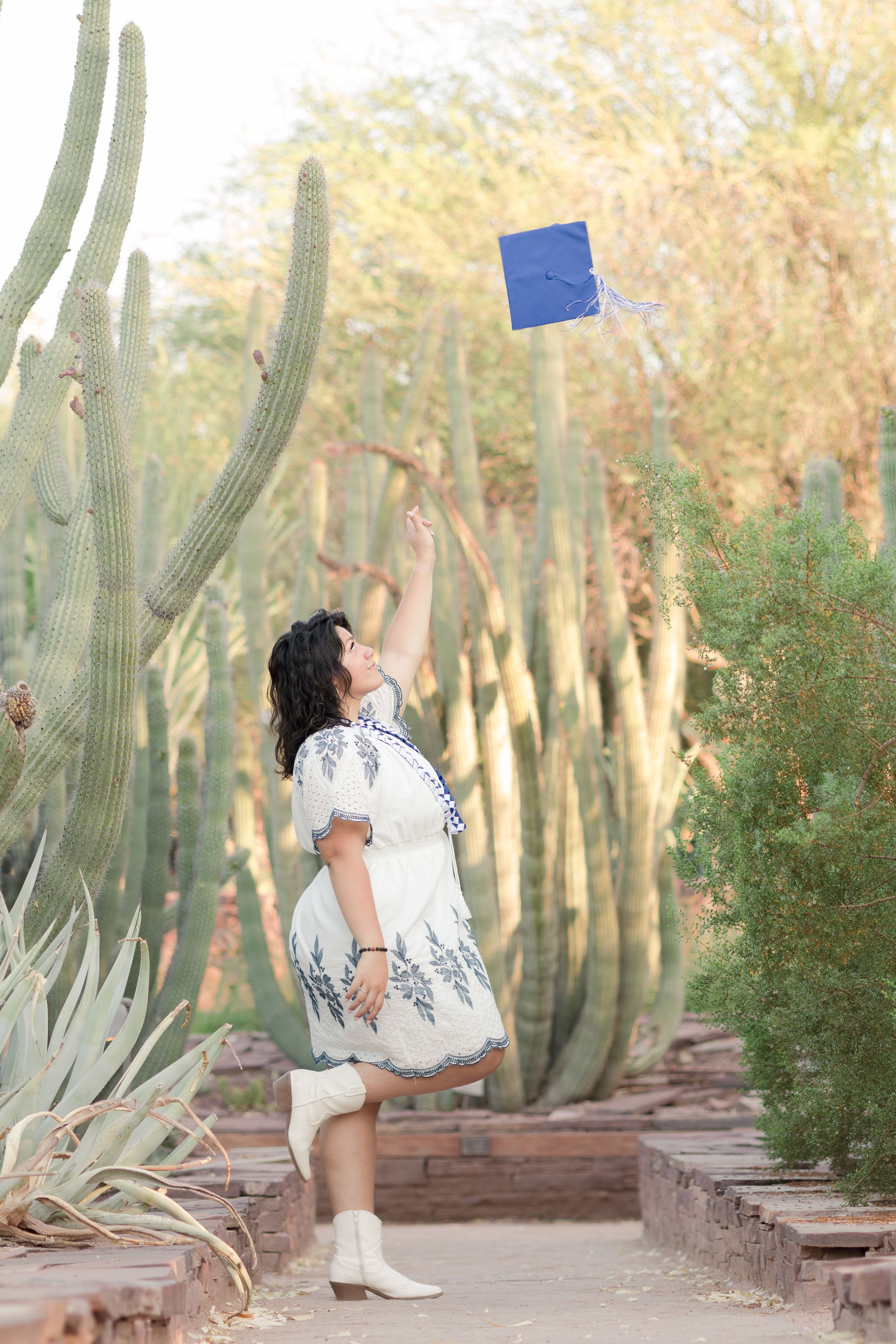 Light and airy senior photo of a girl throwing her graduation cap in the air at the Desert Botanical Garden in Phoenix, Arizona.