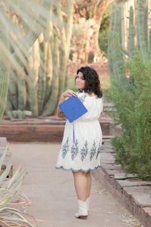 Light and airy senior photo of a girl walking away and looking back with graduation cap in the Desert Botanical Garden in Phoenix, Arizona.