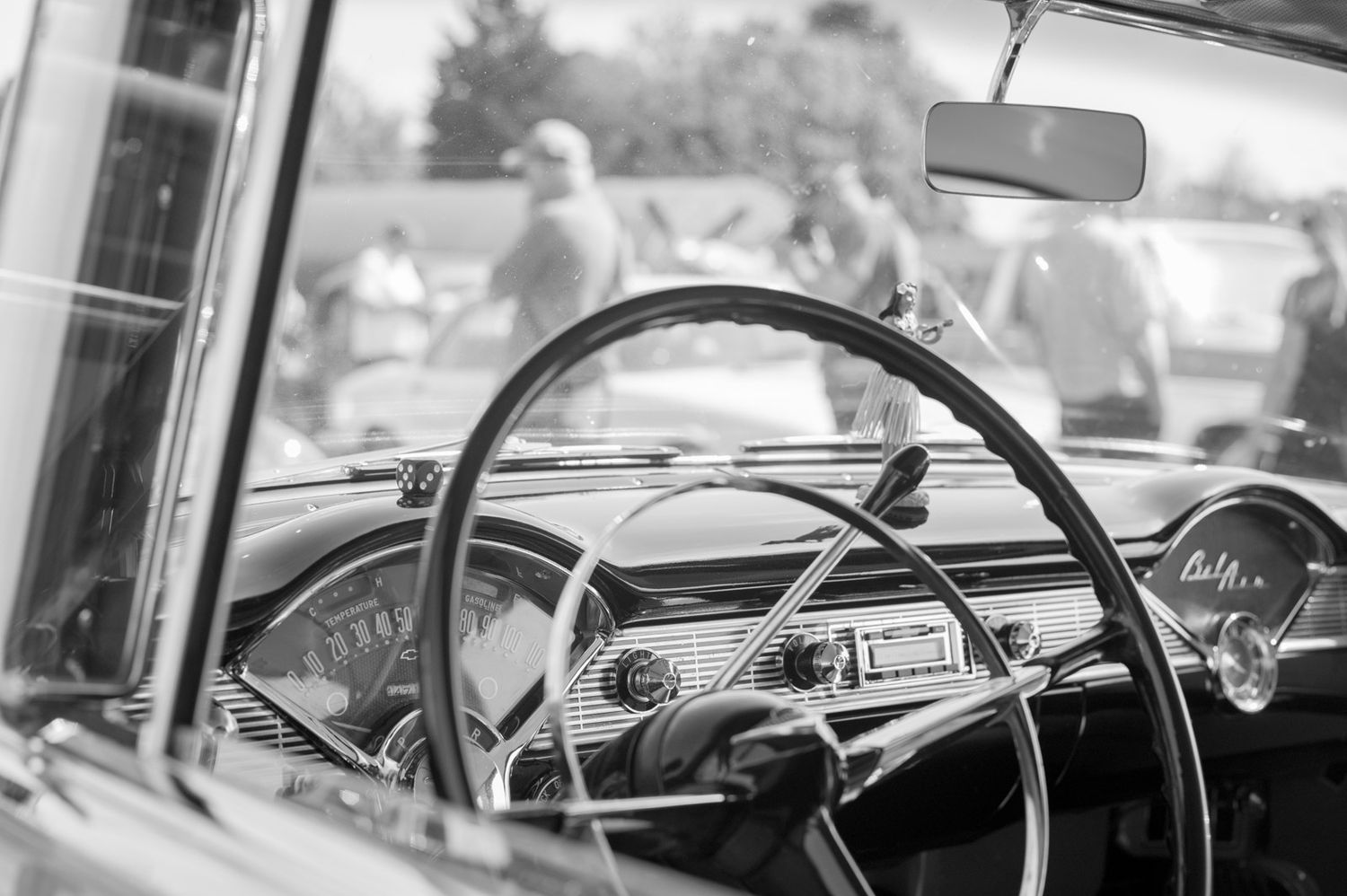 Classic car dashboard and steering wheel shown in black and white with vintage gauges and chrome details.