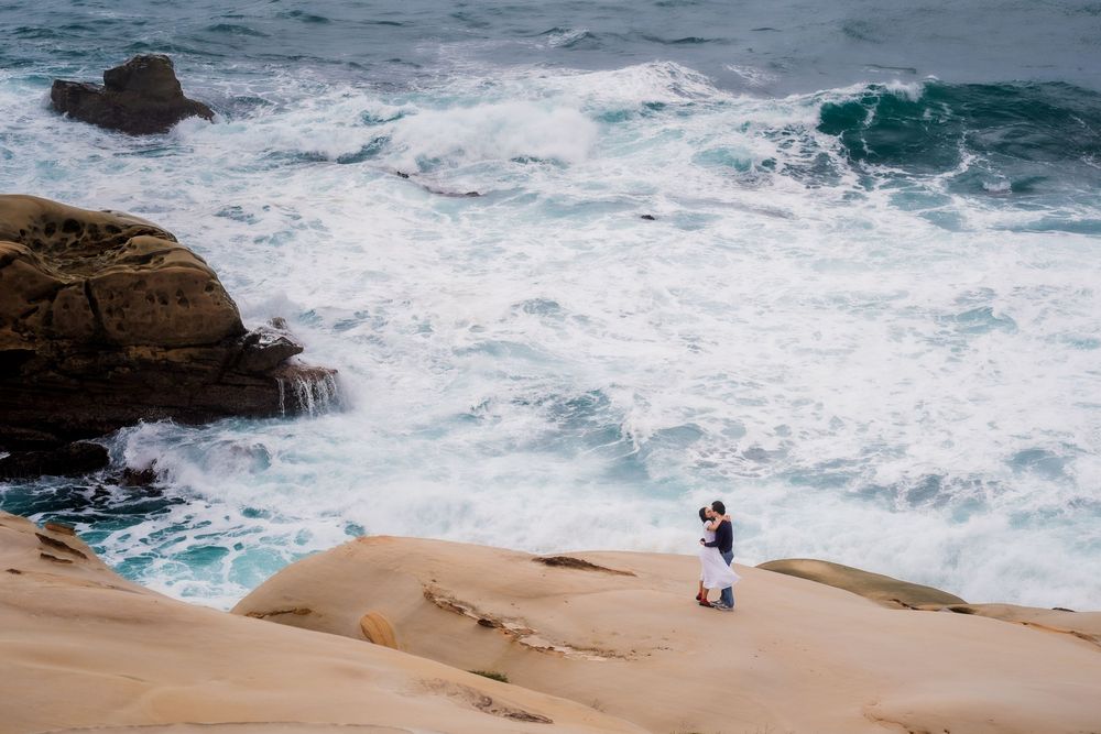 Dramatic ocean waves crashing against rocky coastal cliffs under cloudy skies.