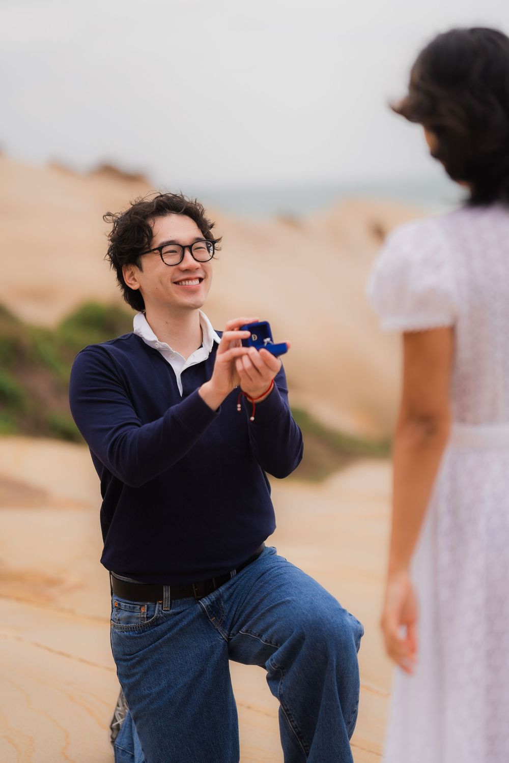 A romantic proposal moment on a sandy beach with ocean views.