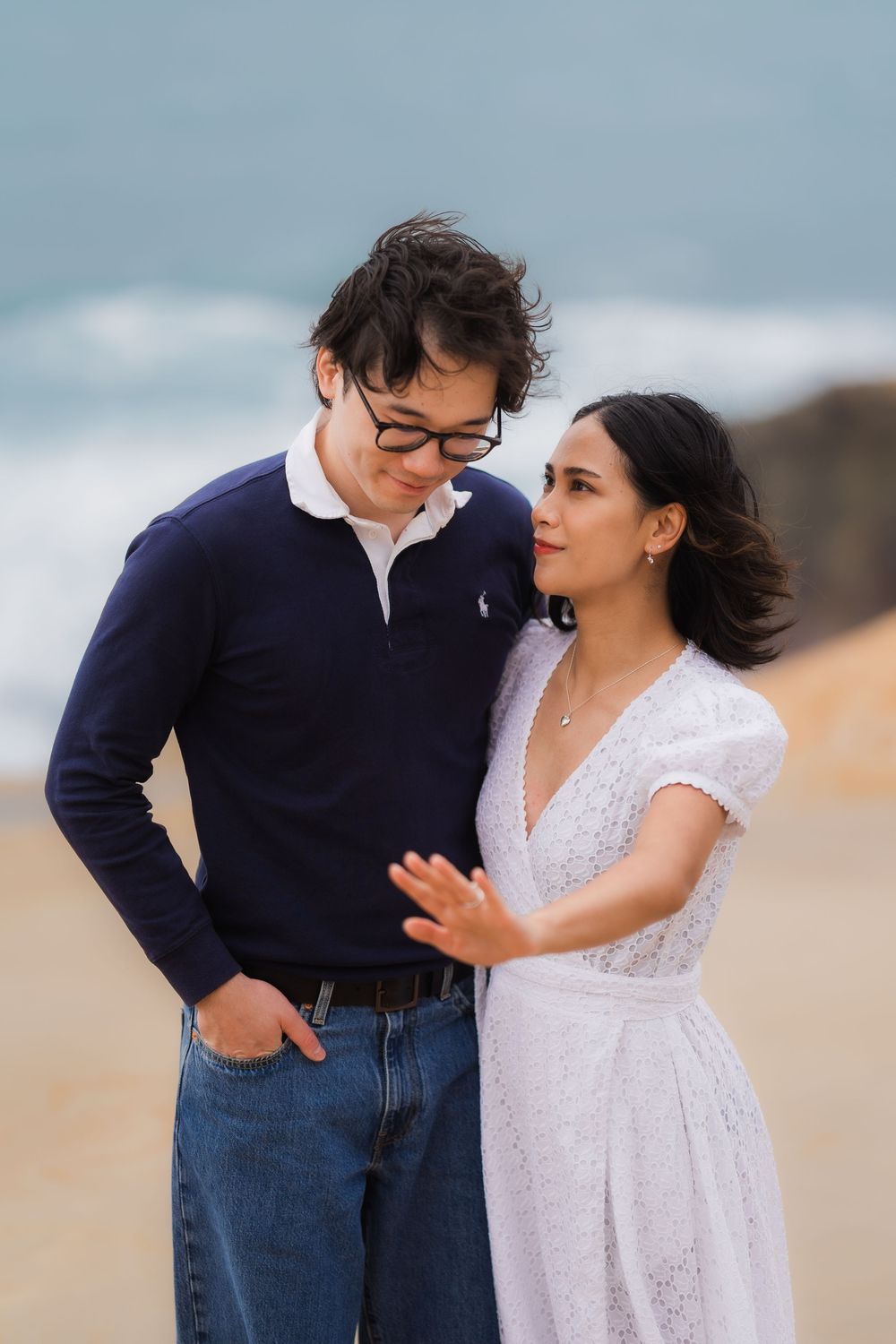 A couple shares a romantic moment on a beach wearing navy and white outfits.