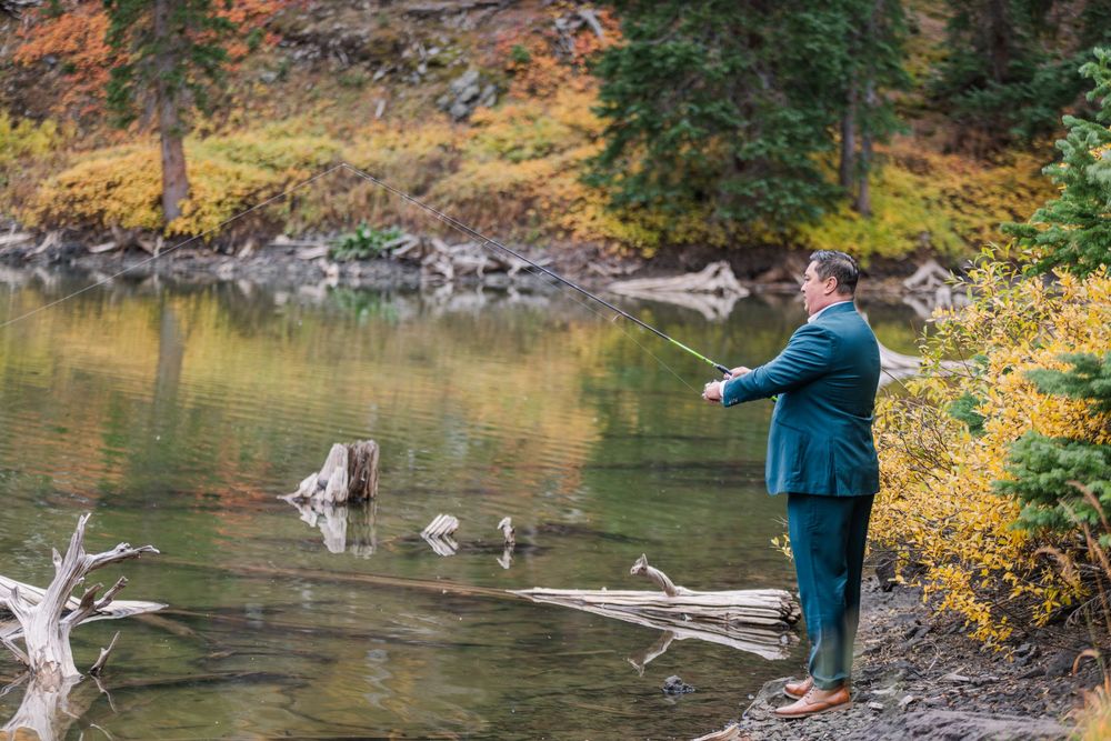 A man in a blue suite and dress shoes is fishing on the edge of a high alpine lake in Autumn in the mountains by Telluride.