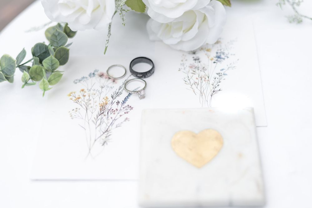 Wedding rings and delicate white flowers arranged on white fabric with eucalyptus leaves create an elegant bridal flatlay.