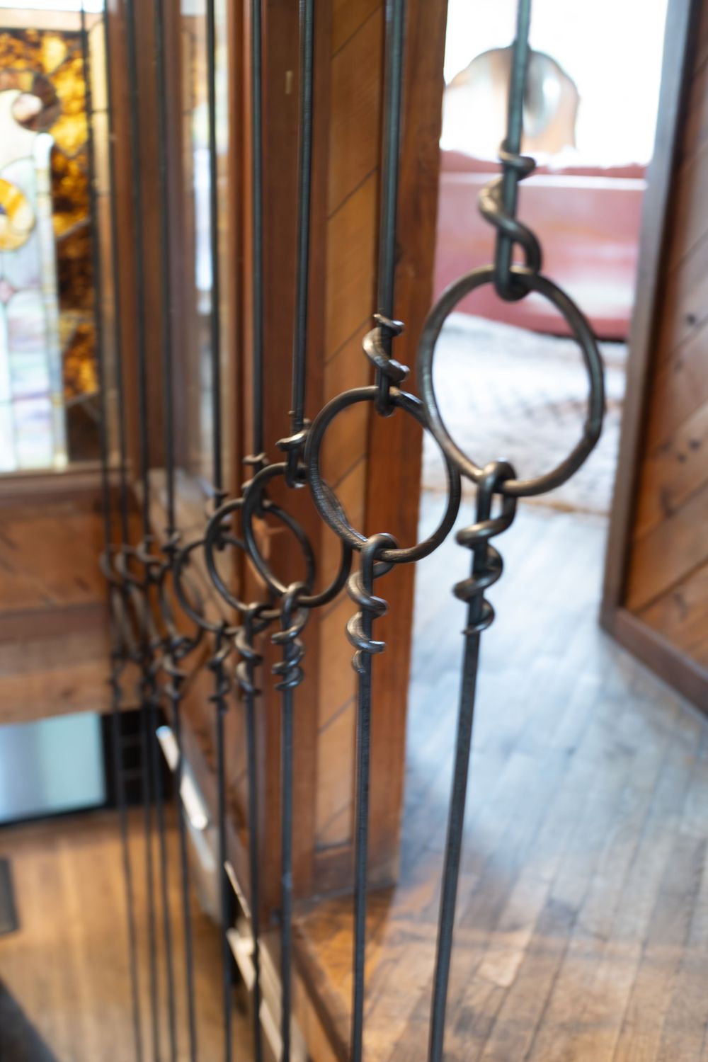 Decorative wrought iron hooks hang in a row along a wooden wall in a rustic cabin with wood floors.