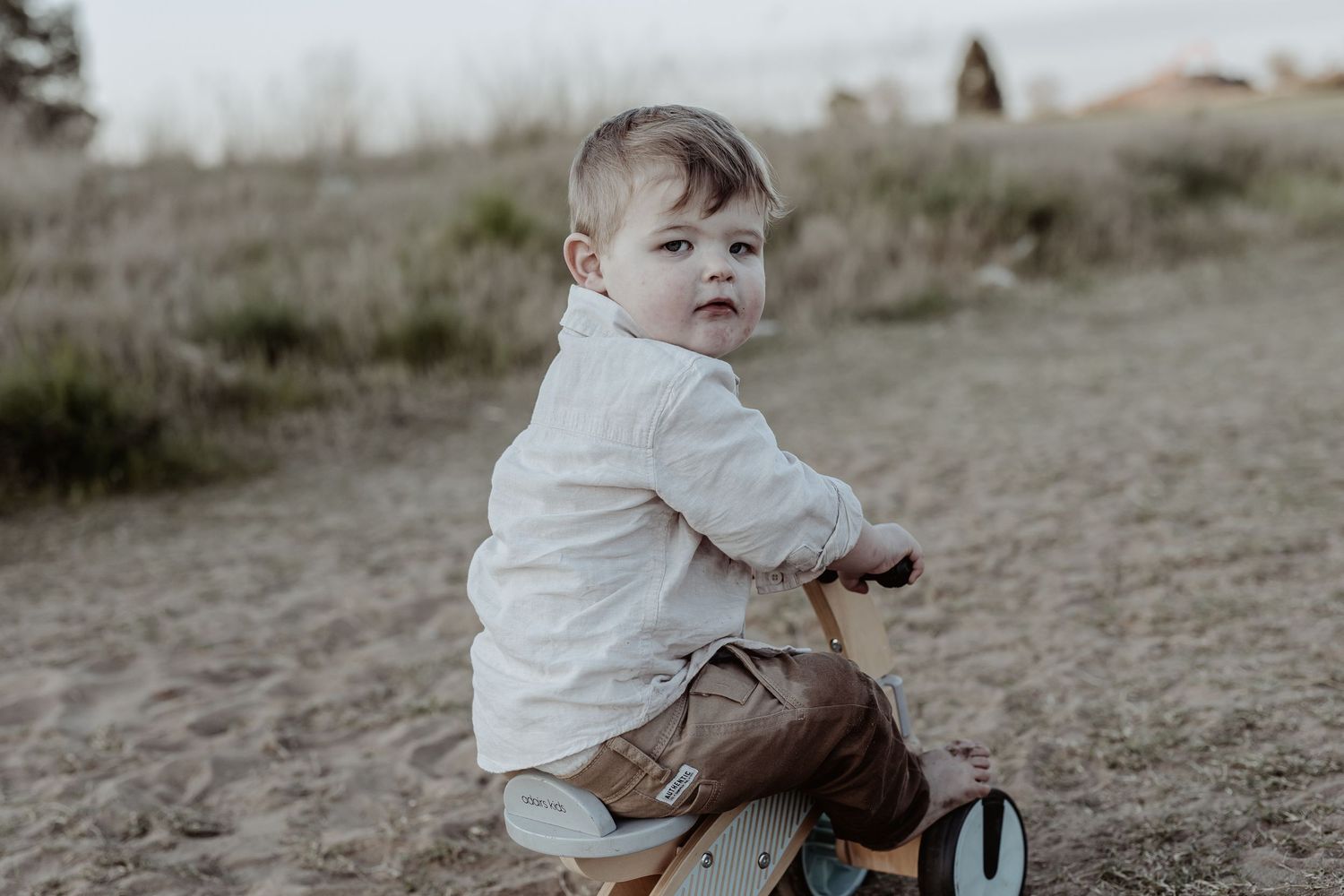 Child sitting alone in a field wearing white clothing during sunset.