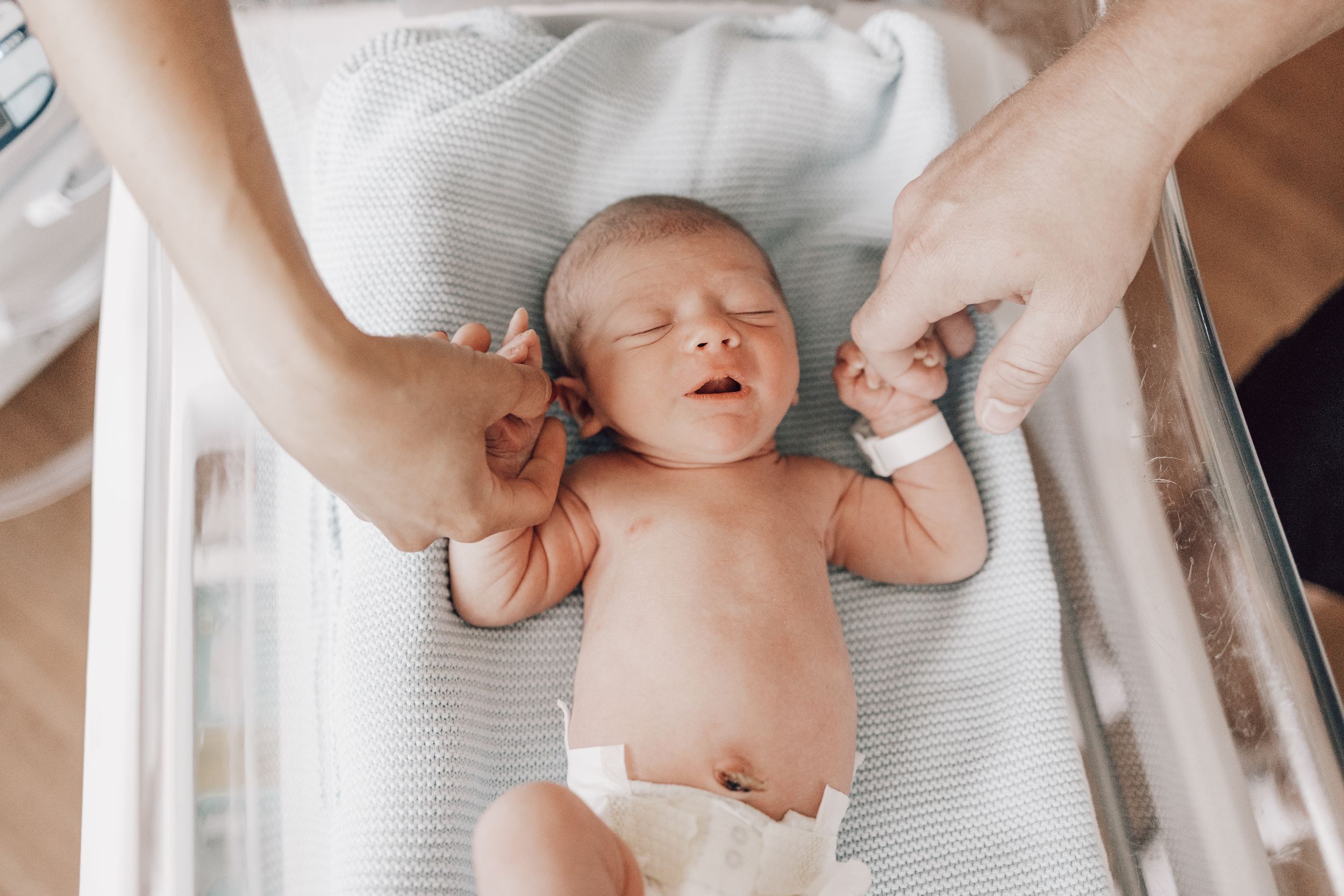 A newborn baby lies on a white blanket while being gently massaged during an infant massage session.