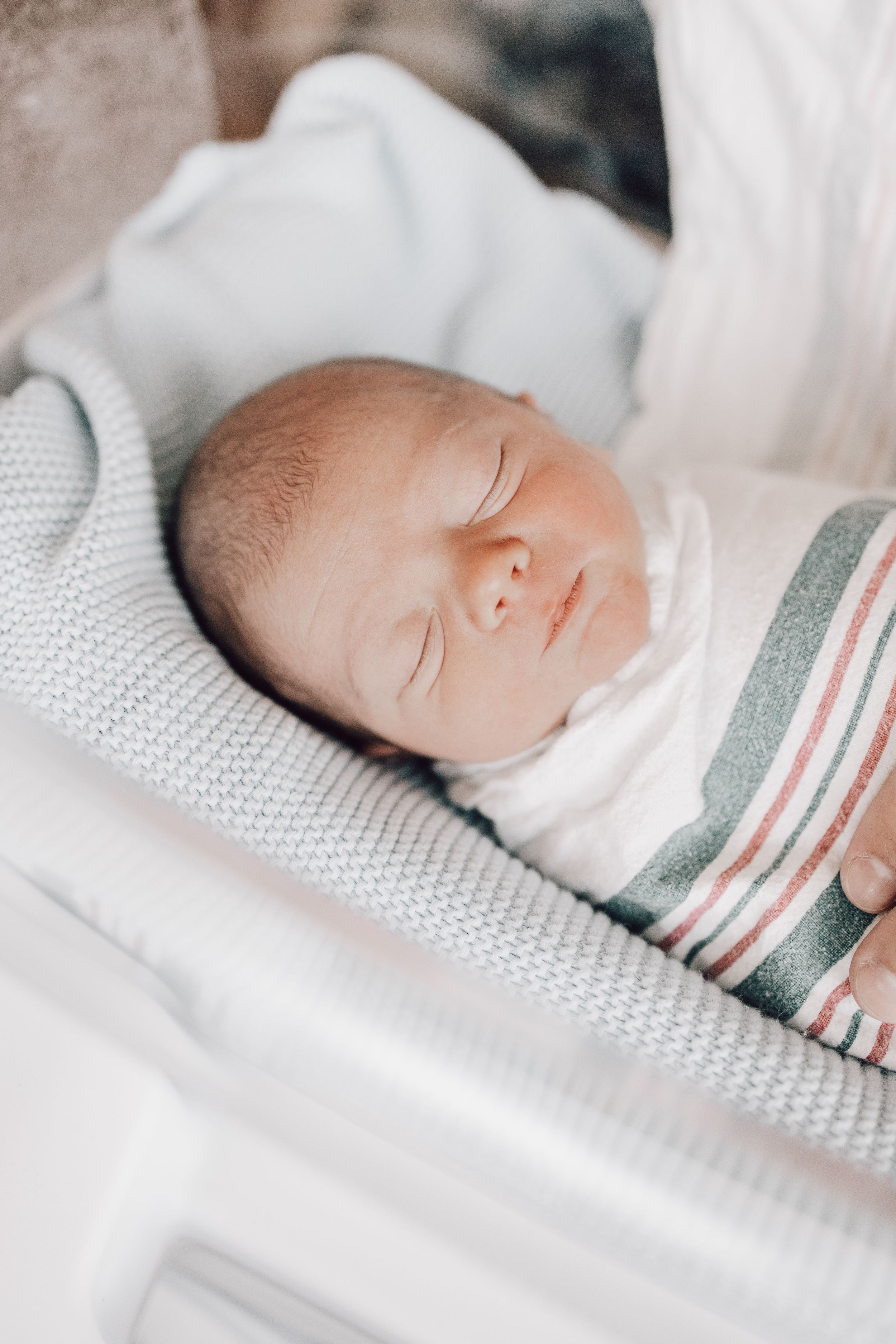 Newborn baby sleeping peacefully on white textured bedding with a striped blanket.