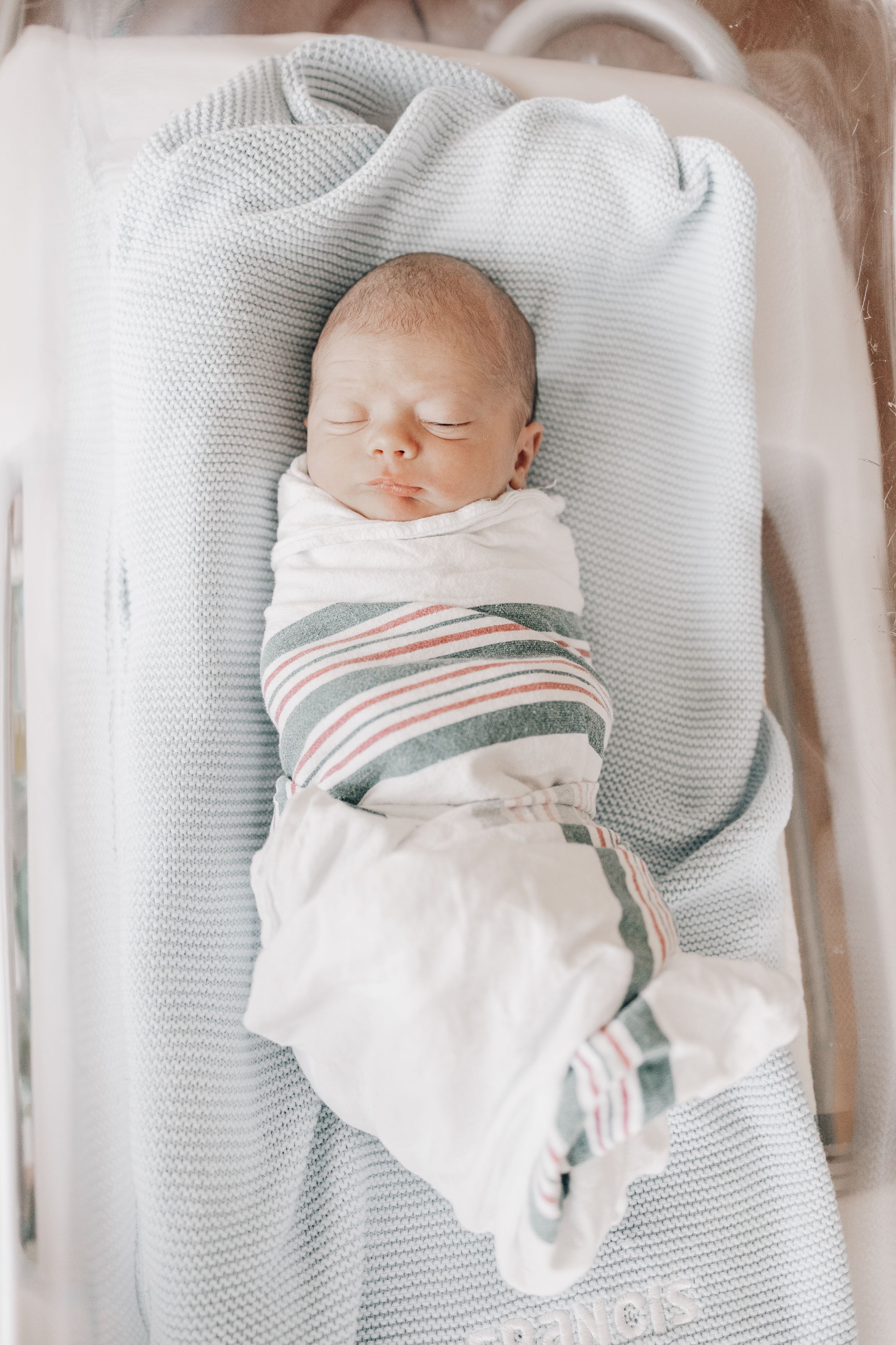 Swaddled newborn resting on a knitted blanket wearing a striped outfit.