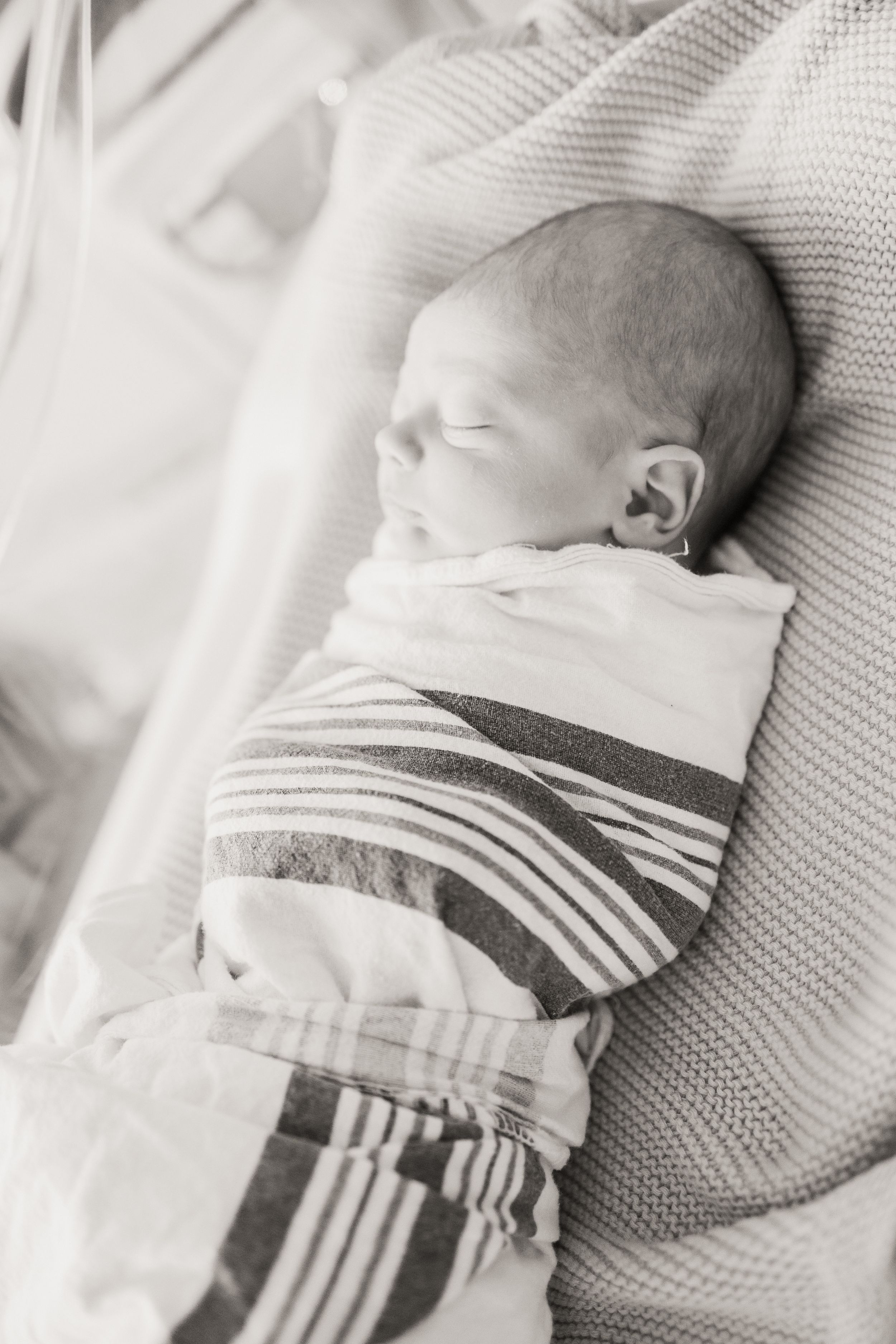 A sleeping newborn baby swaddled in a striped blanket lies peacefully on white bedding.